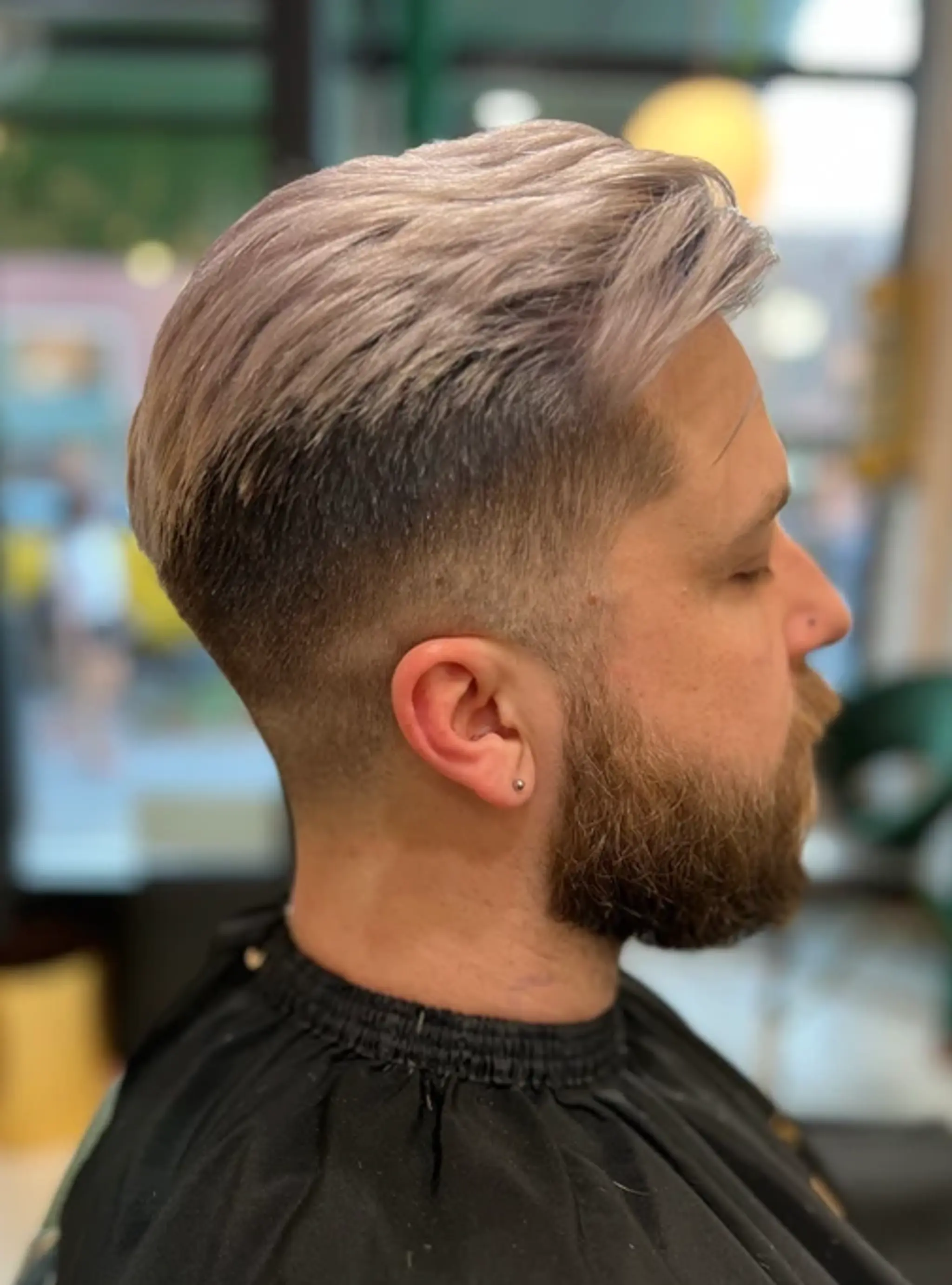 A short, side-swept haircut with a low fade and a longer, textured top in a silver and ash blonde color.