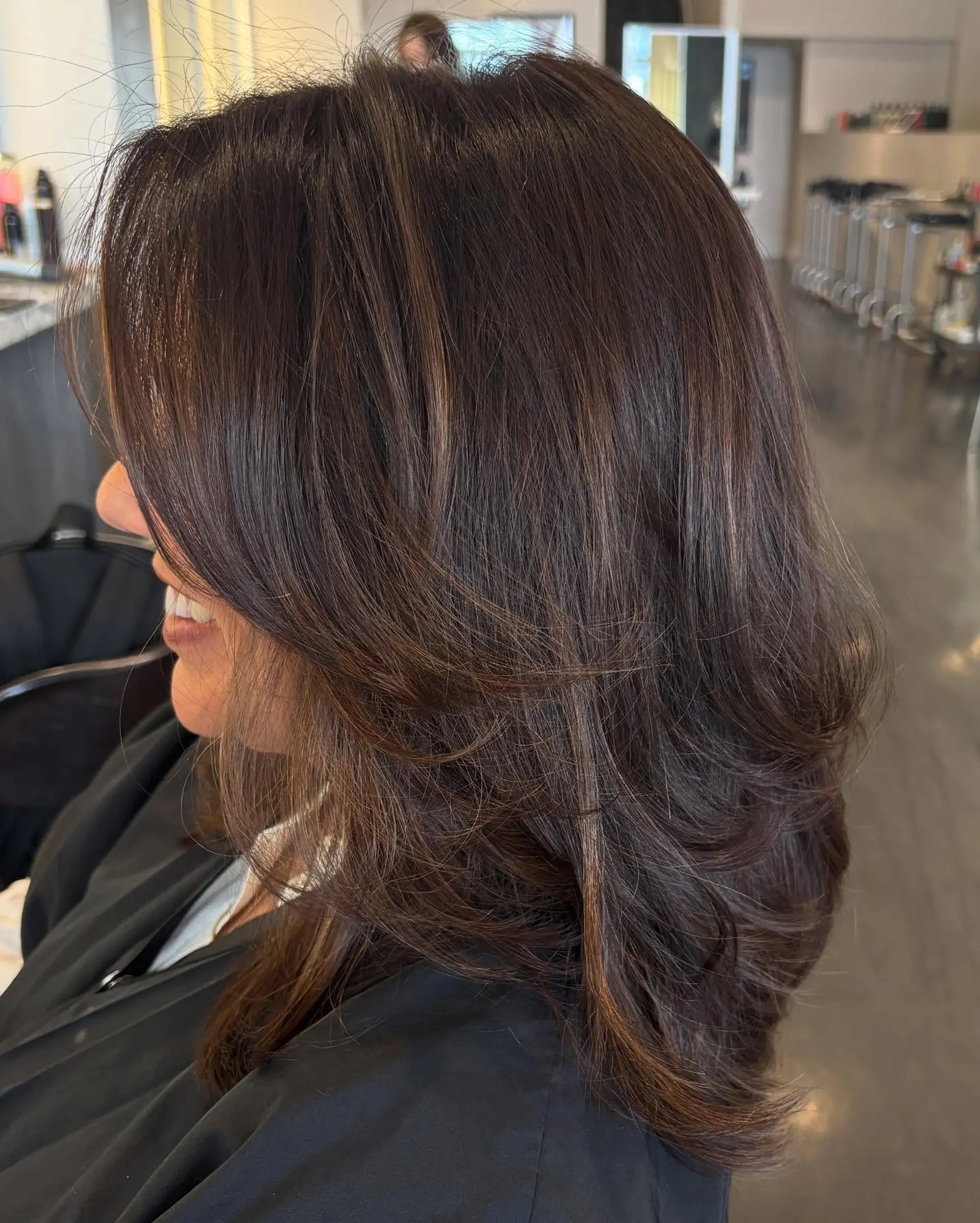 A dimensional chocolate brown blowout featuring soft, cascading layers that frame the face with smooth movement. 1