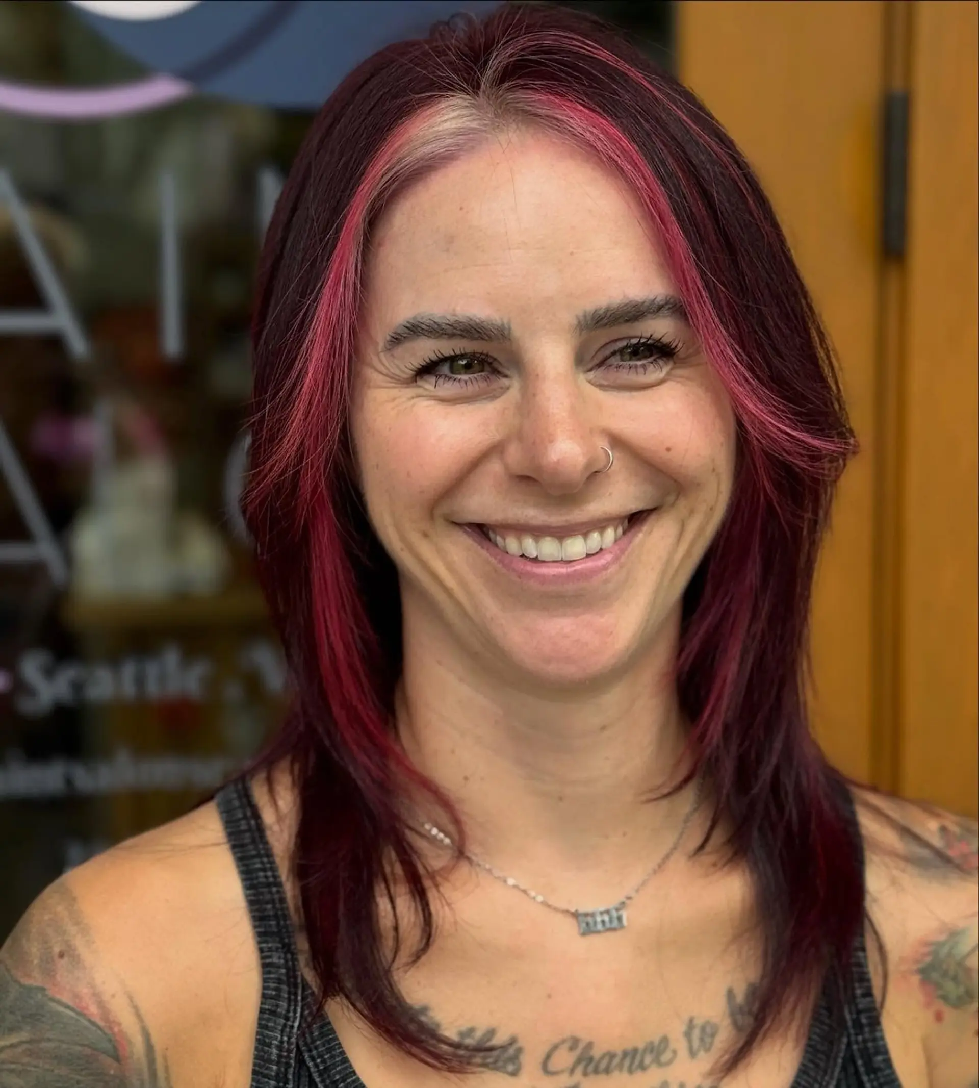 A medium-length layered haircut with a deep plum base and a bright magenta-pink money piece. 1