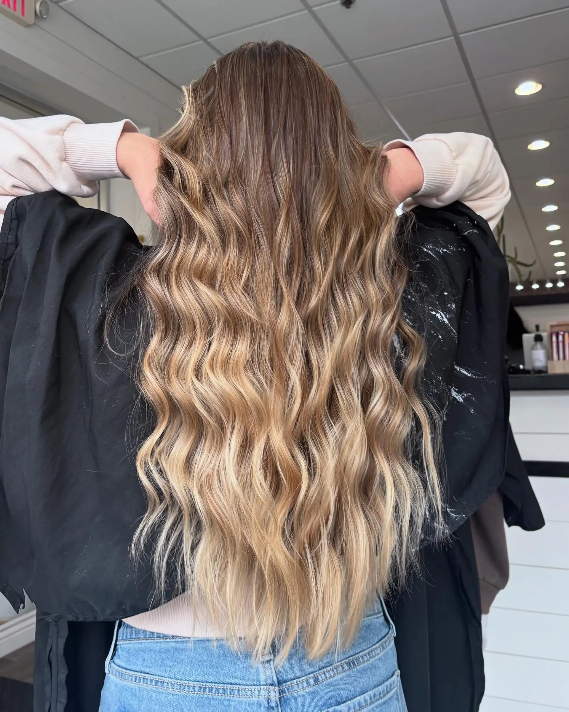 Long hair featuring a seamless dimensional blend of light brown and honey blonde styled in textured waves. 1