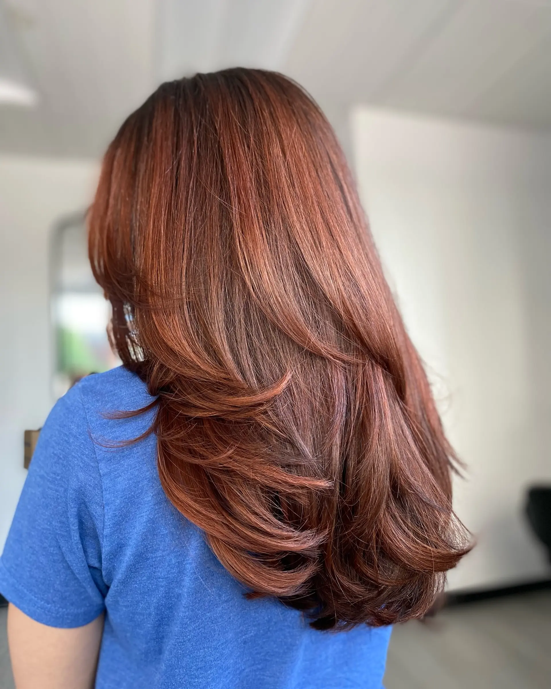 Long auburn hair styled with smooth, cascading curved layers and a voluminous blowout finish. 1