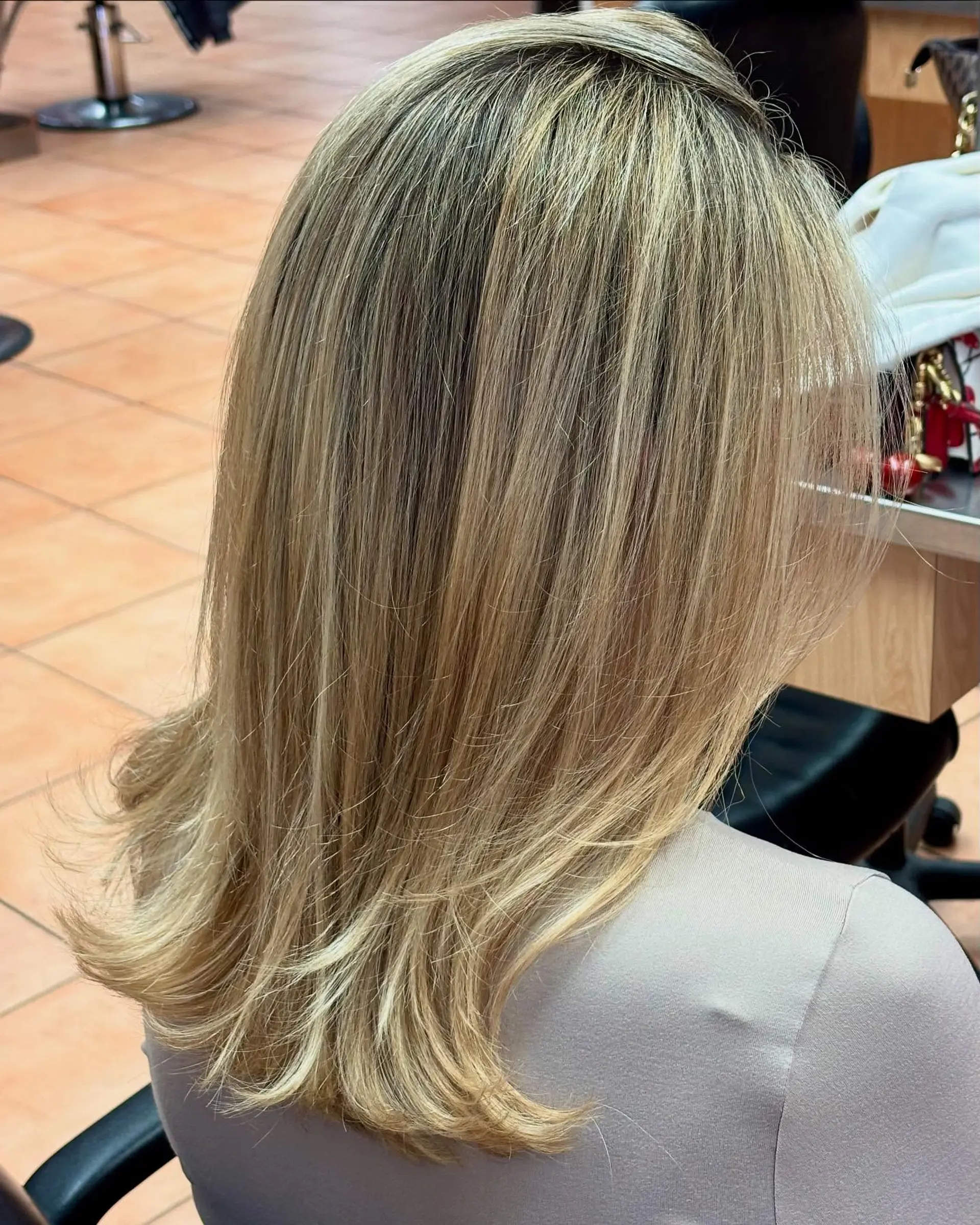 A medium-length layered blonde haircut styled with a smooth finish and softly flipped ends. 1