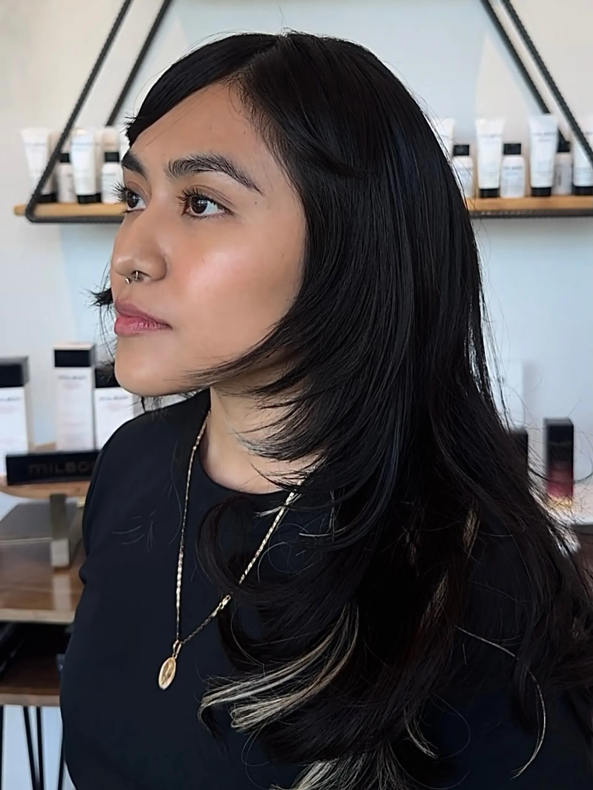 Long black layered haircut with sweeping side bangs, face-framing layers, and blonde peekaboo streaks. 1