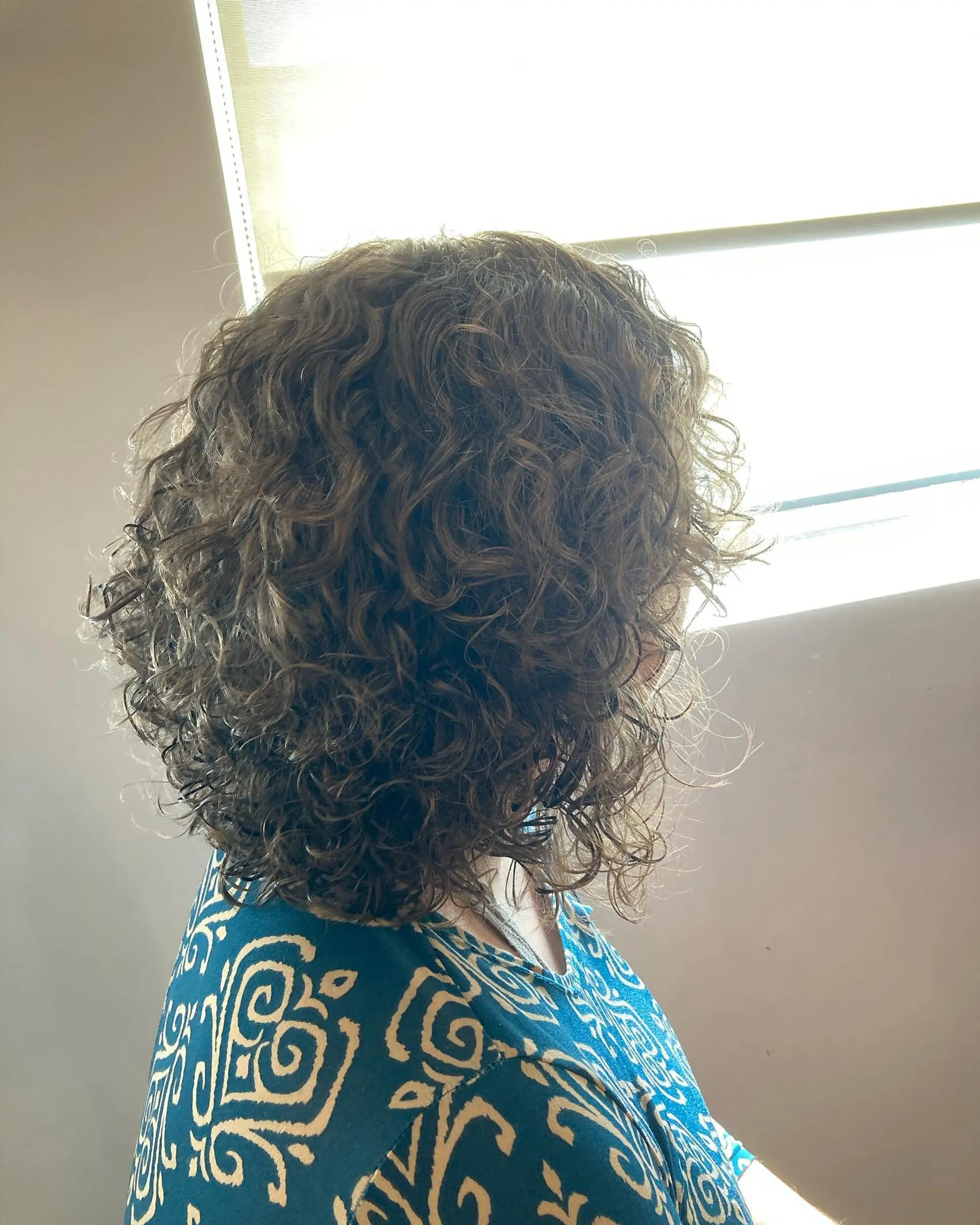 A shoulder-length layered haircut tailored for natural curls to enhance shape, volume, and bounce. 1