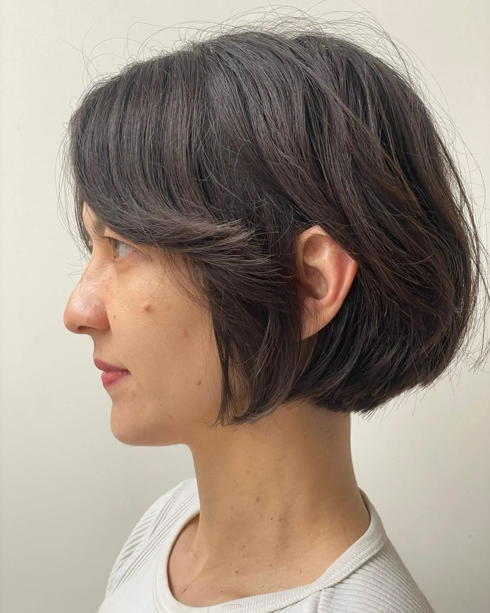 A chic asymmetrical short bob with straight dark brown hair, featuring subtle volume and tucked behind the ear for a graceful look. 1