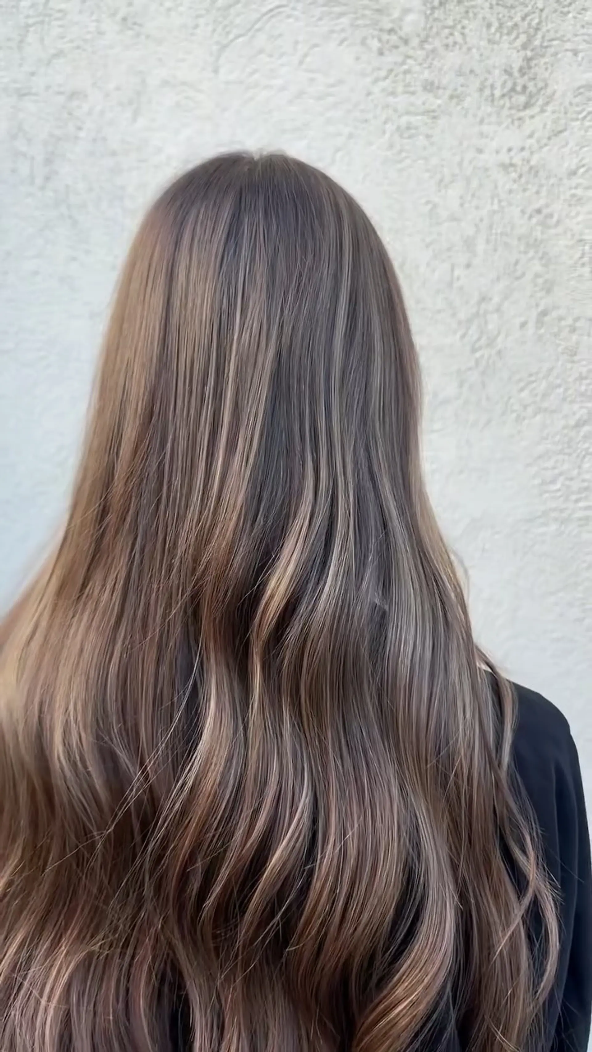 Long dimensional brunette hair with soft lived-in balayage highlights styled in gentle waves. 1