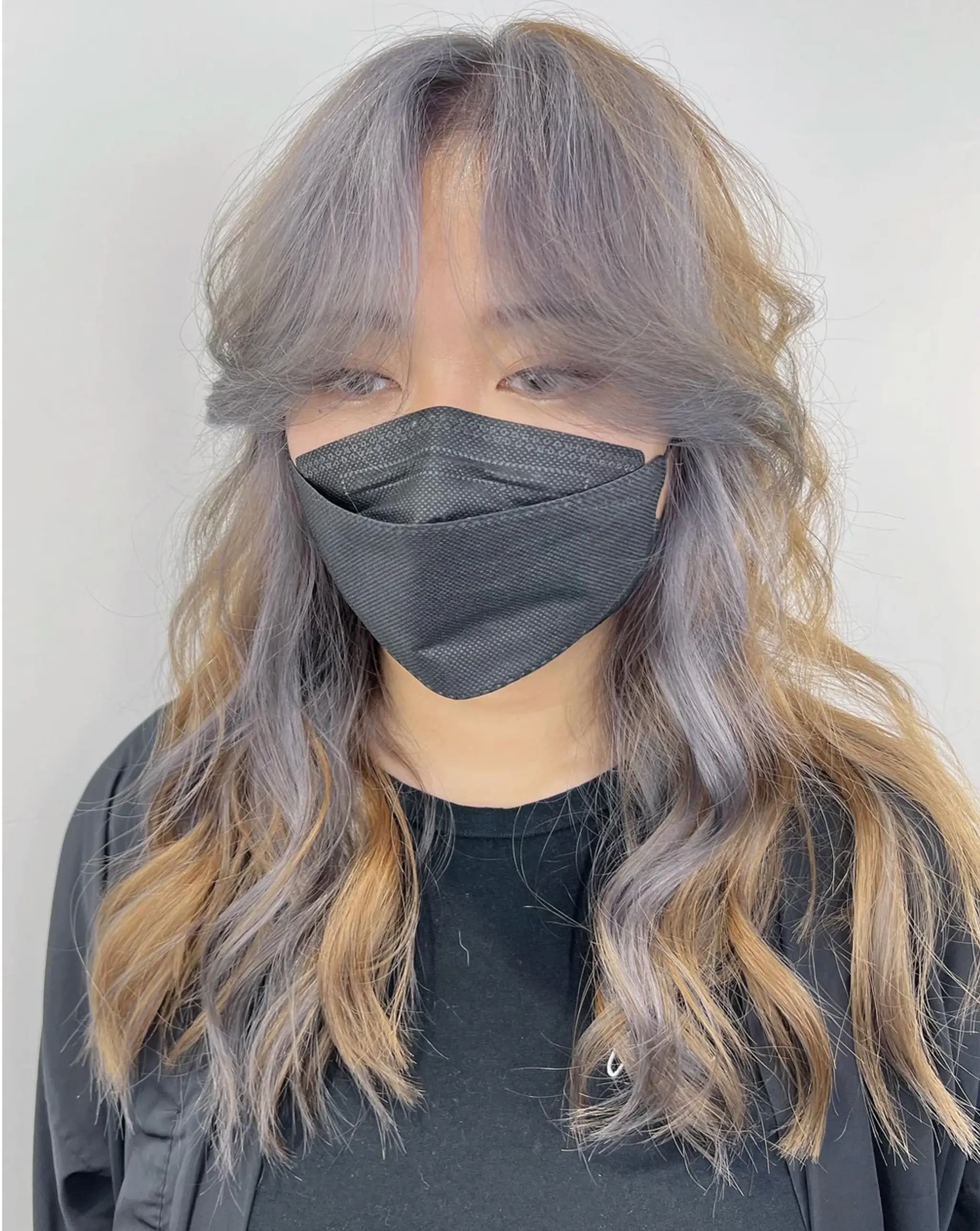 Long, wavy lilac hair with face-framing bangs, fading into honey blonde and ash grey, with a middle part and voluminous waves.