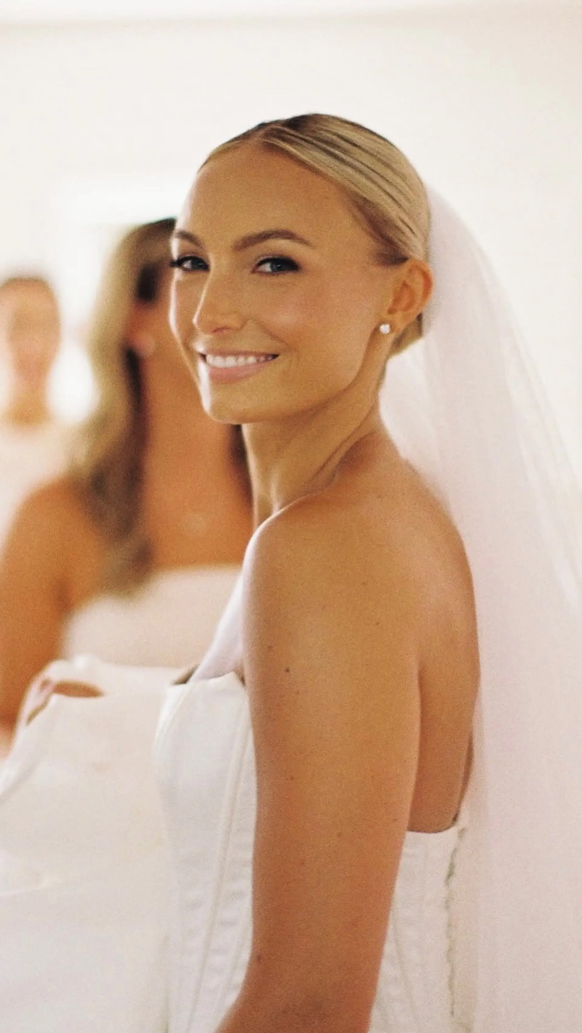 A sleek, center-parted low bridal bun styled smoothly back and secured at the nape, paired with a classic wedding veil. 1