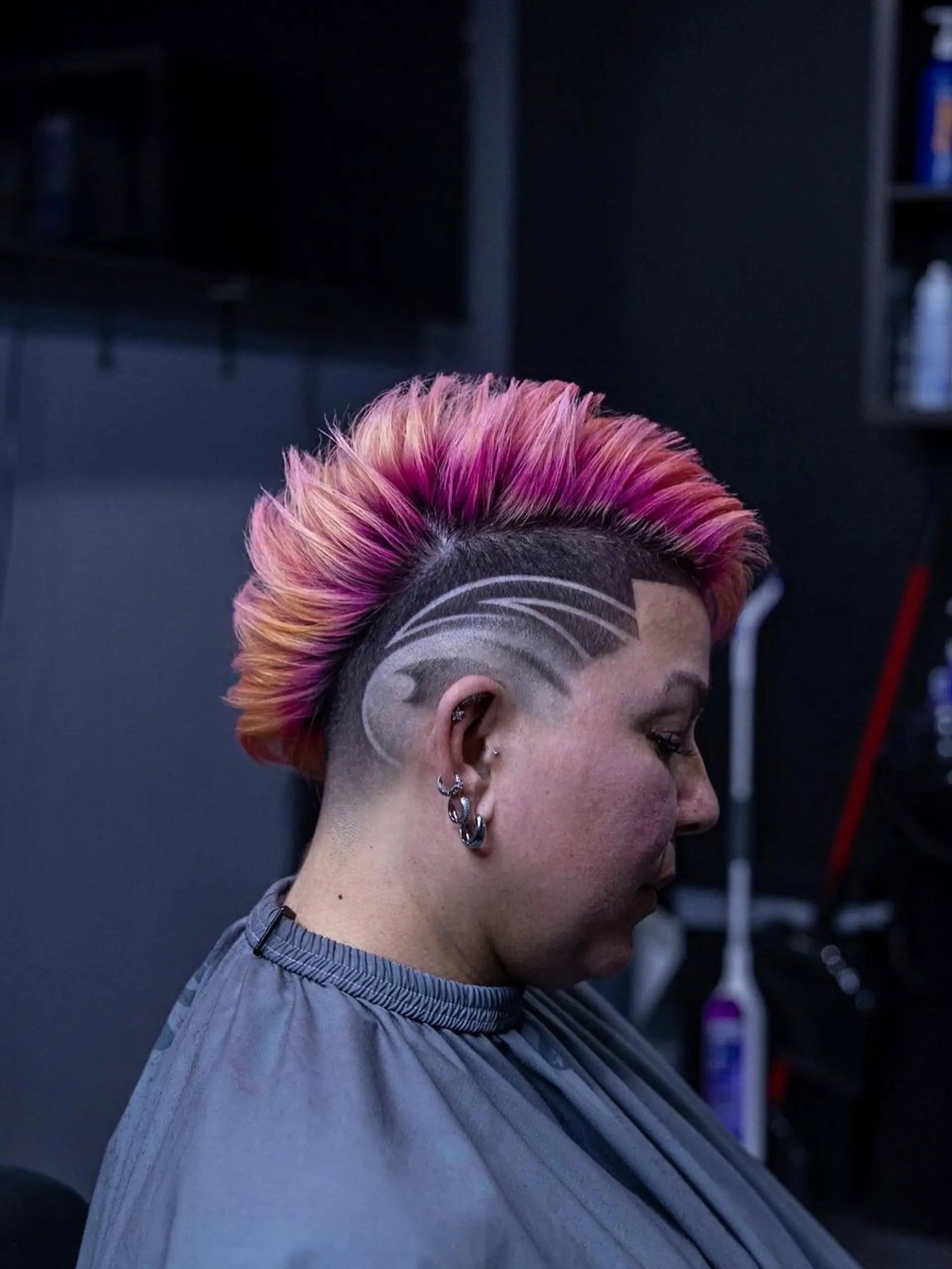 A vibrant pink and peach textured mohawk paired with closely shaved sides showcasing a curved hair design. 1