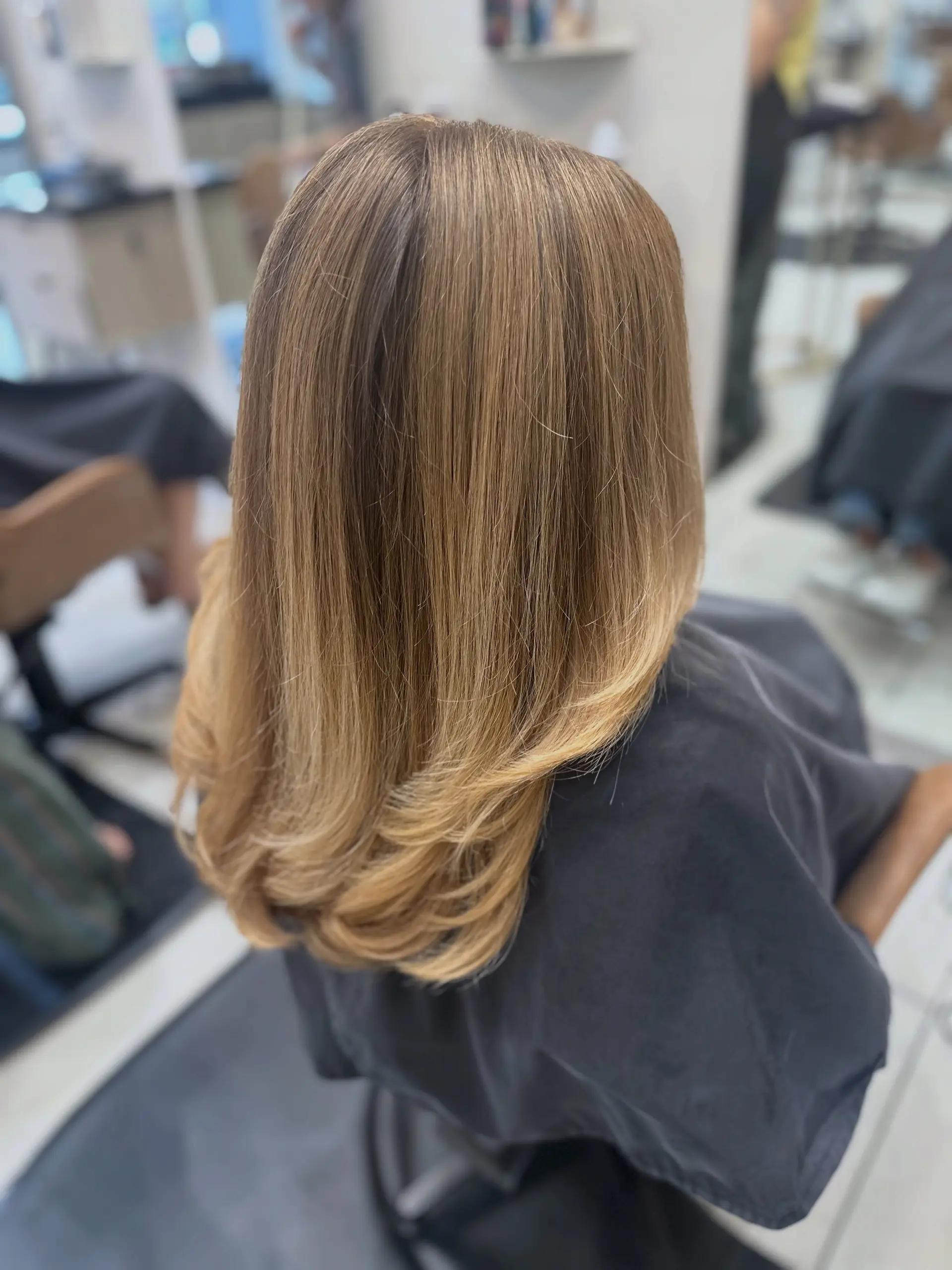 Long honey blonde hair featuring soft layers and a smooth blowout with ends turned under. 1