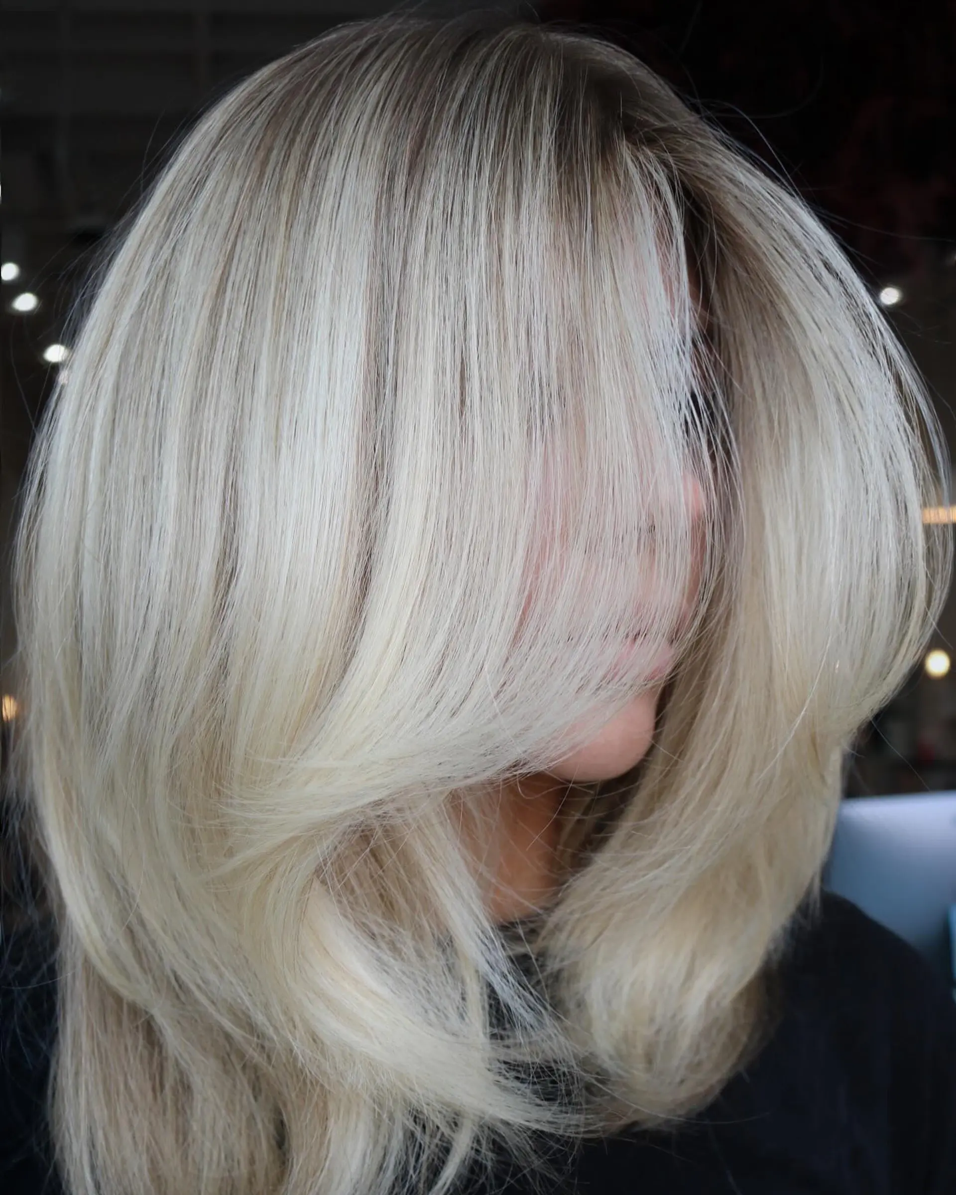 A bright neutral blonde medium-length haircut styled in a full, voluminous blowout with sweeping face-framing layers. 1