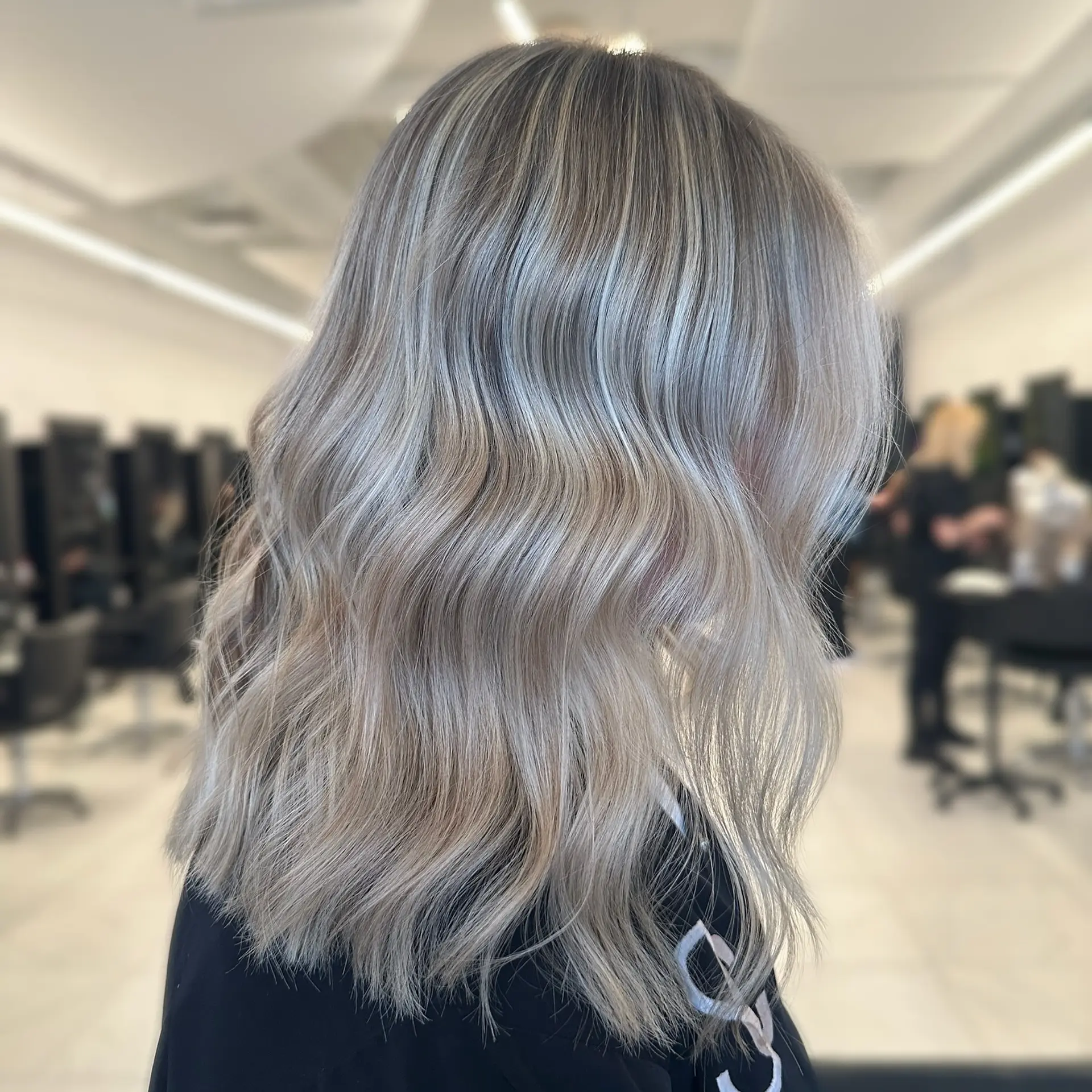 Medium-length ash blonde hair styled in soft, textured waves with a seamless root melt and dimensional highlights. 1