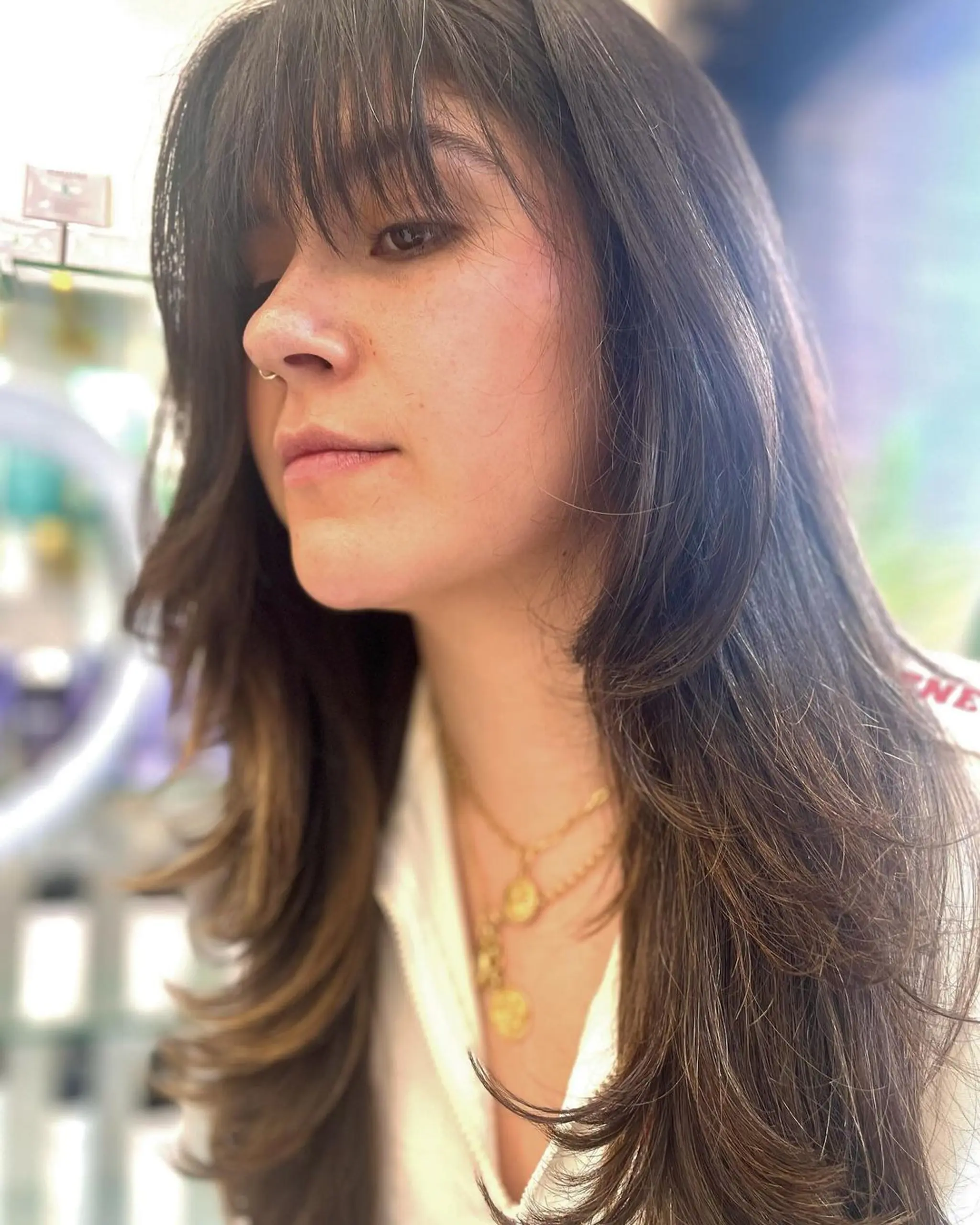 The hairstyle features long, dark brown straight hair with soft light brown highlights. Its defining elements include a full fringe and elegant, soft layers that transition into feathered ends, with face-framing layers adding a touch of sophistication. 1
