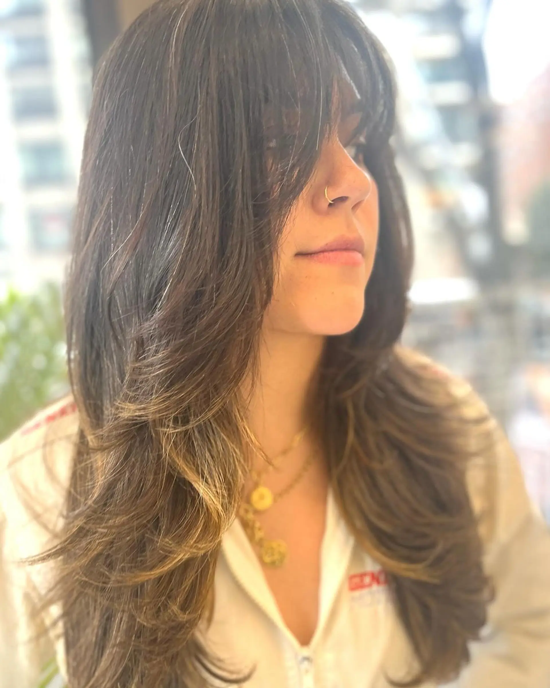 The hairstyle features long, dark brown straight hair with soft light brown highlights. Its defining elements include a full fringe and elegant, soft layers that transition into feathered ends, with face-framing layers adding a touch of sophistication. 2