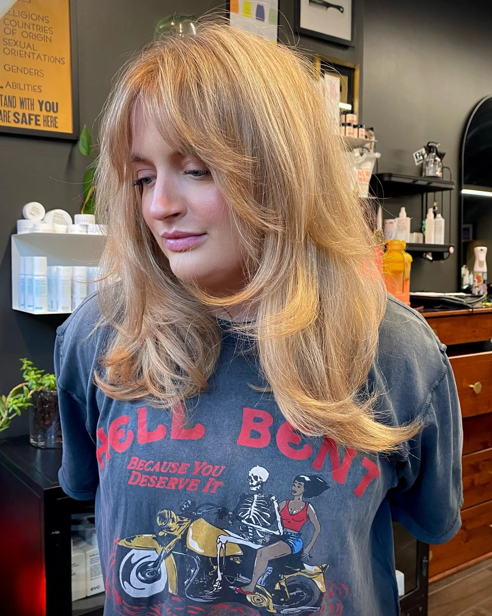 A layered long cut featuring wispy curtain bangs and soft face-framing pieces in a warm strawberry blonde shade. 1