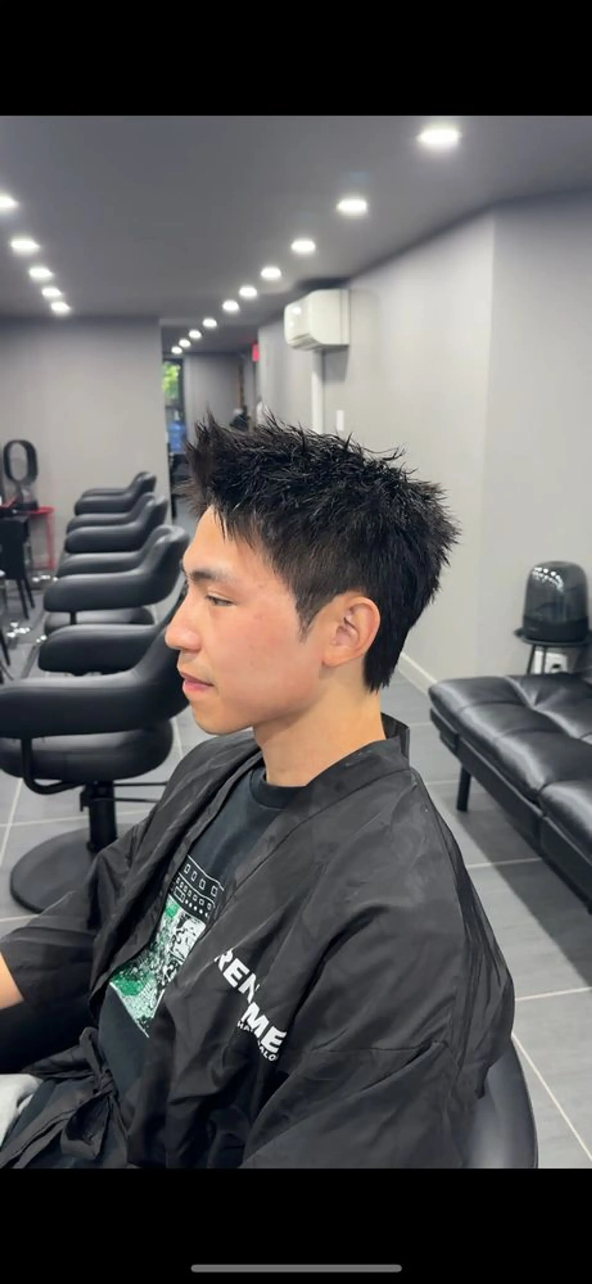 This hairstyle features a modern, edgy look with straight, short black hair styled into sharp spikes. The overall texture is choppy and filled with volume, giving it a dynamic and contemporary appearance. The sides are faded, adding to the sleek and clean aesthetic. Down perm used on the side and perm on the top to accentuate the texture of the cut. 2