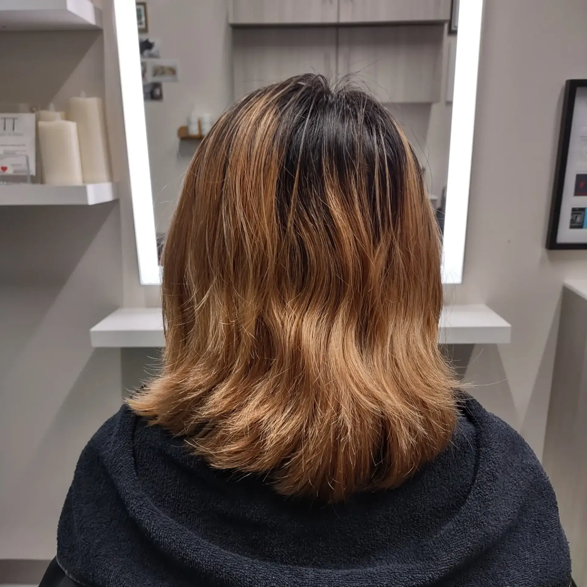 A textured shoulder-length lob featuring soft, flared ends with a natural dark brown root transitioning into warm golden-caramel tones. 1
