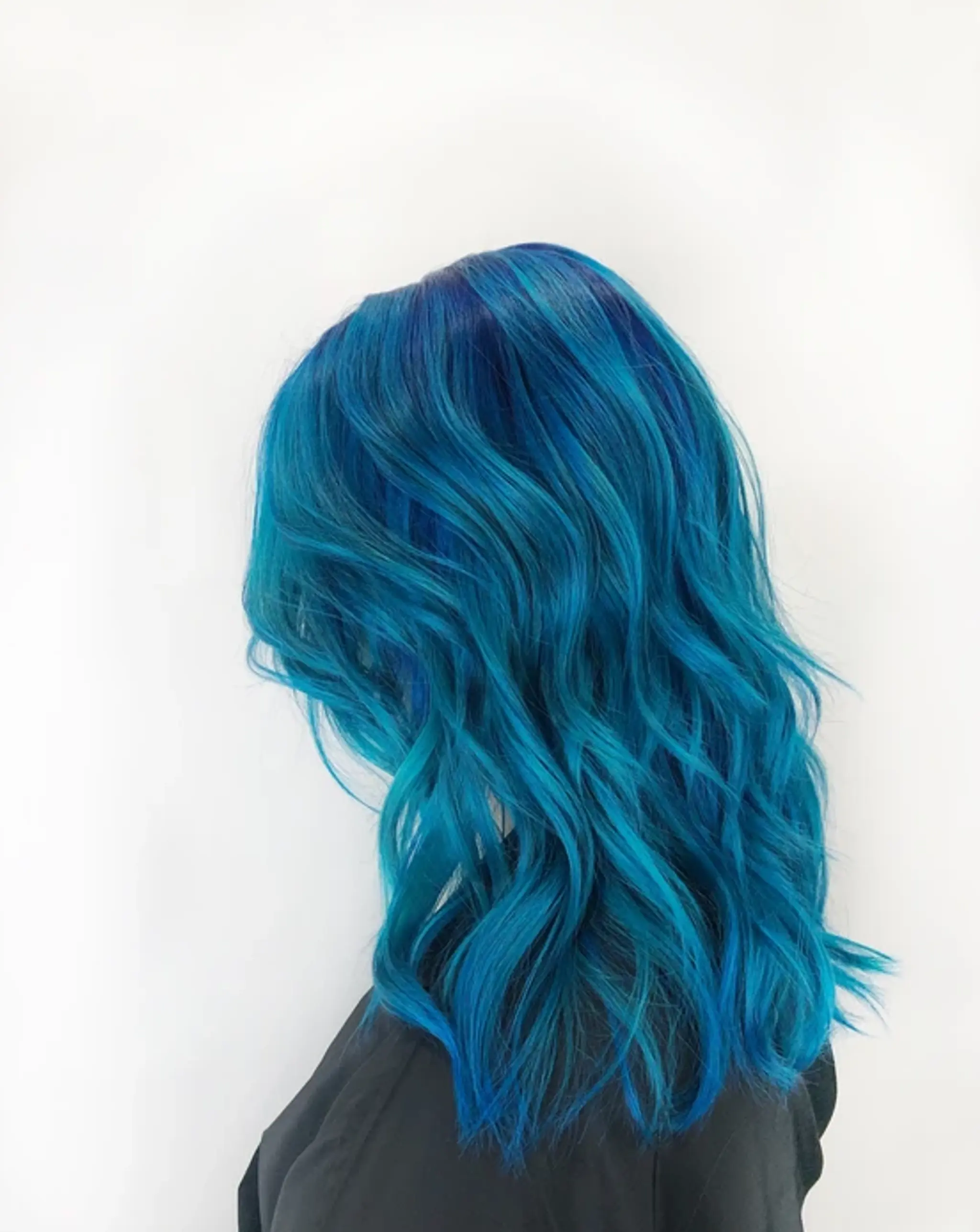 Medium-length wavy hair in vibrant shades of blue, teal, and navy blue, with soft yet defined waves adding volume and movement.