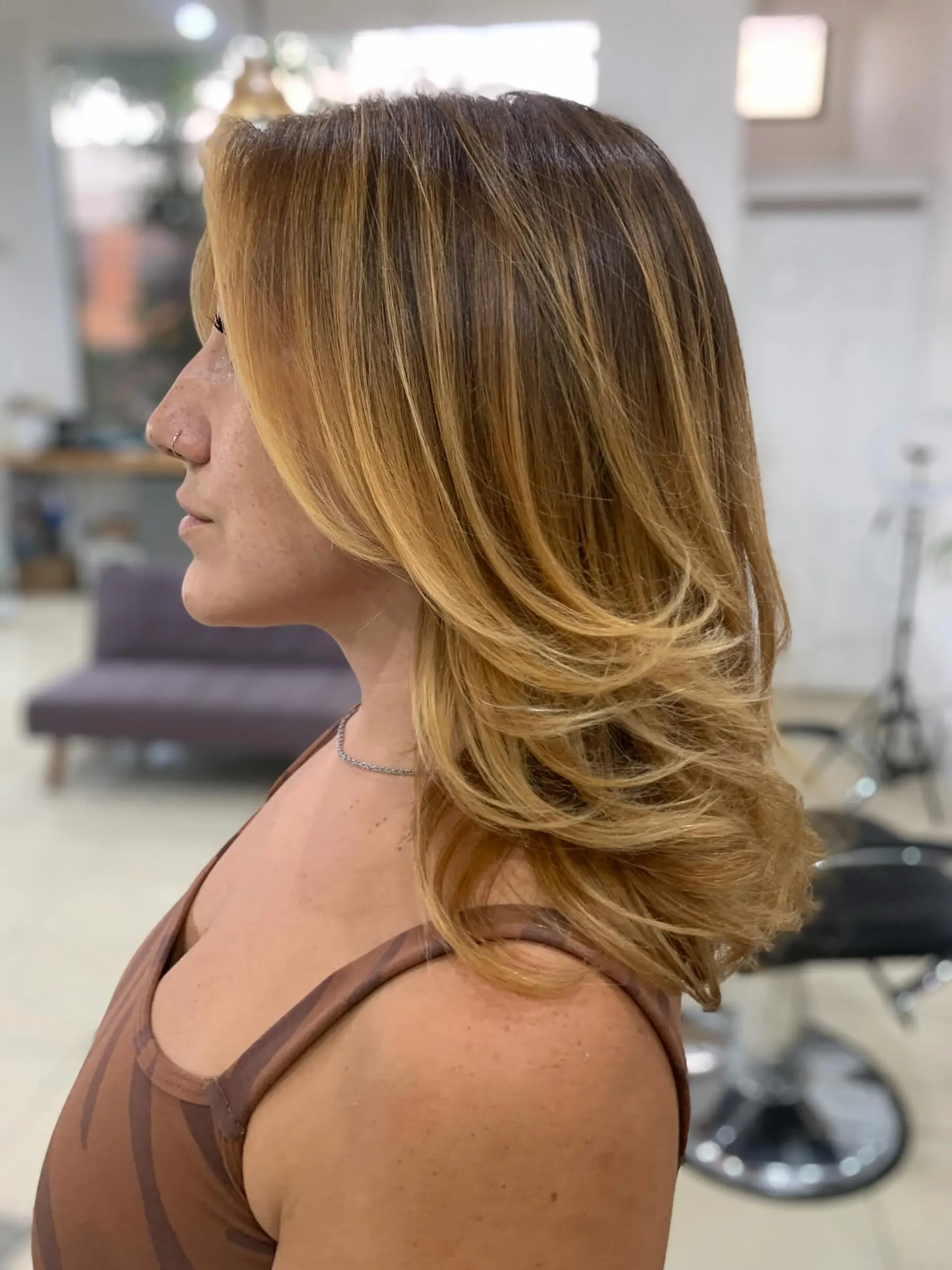Medium-length layered haircut styled with a feather-layered blowout and golden blonde balayage highlights. 1
