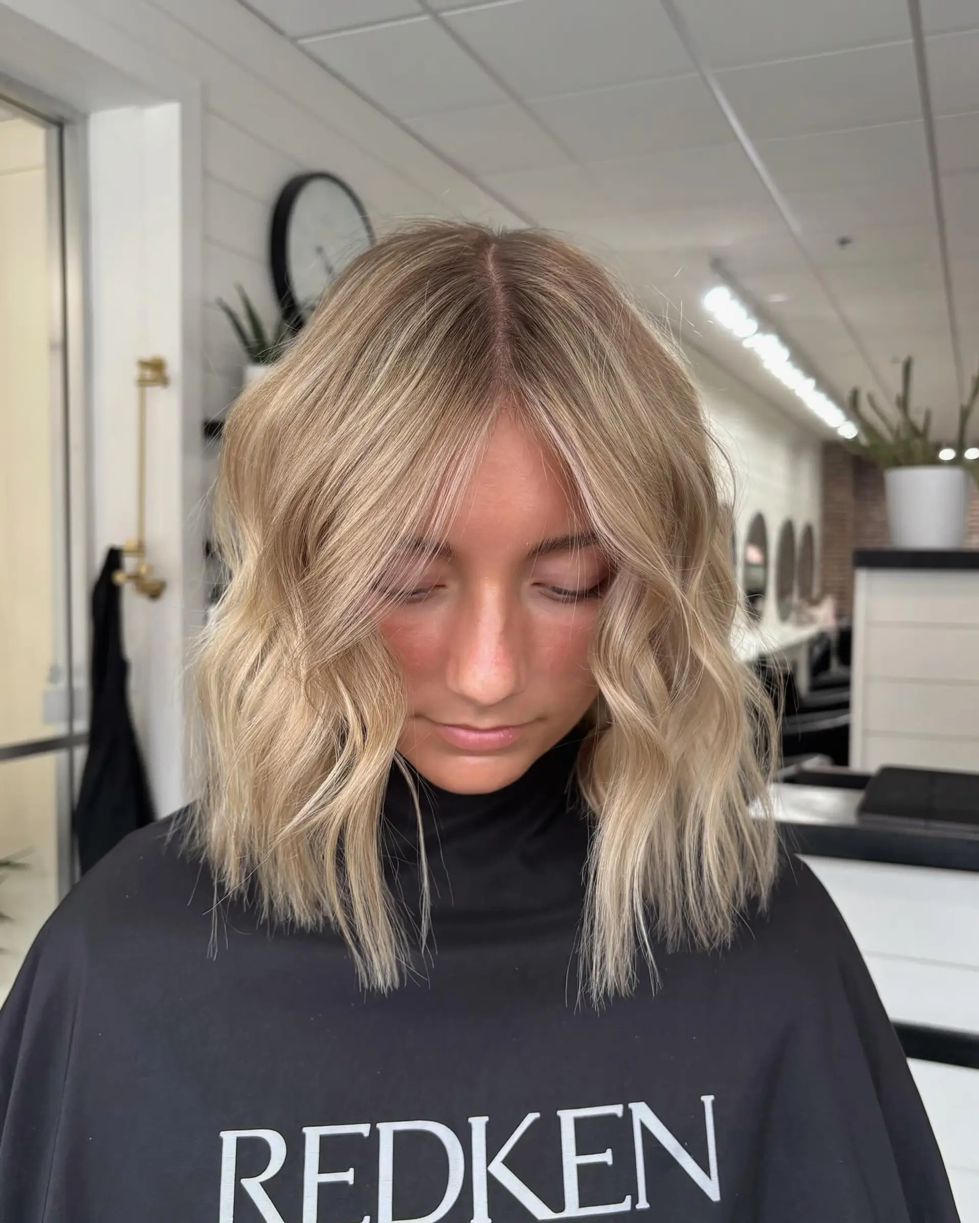 A blunt textured lob with soft waves, featuring bright dimensional blonde highlights and a subtle shadow root. 1