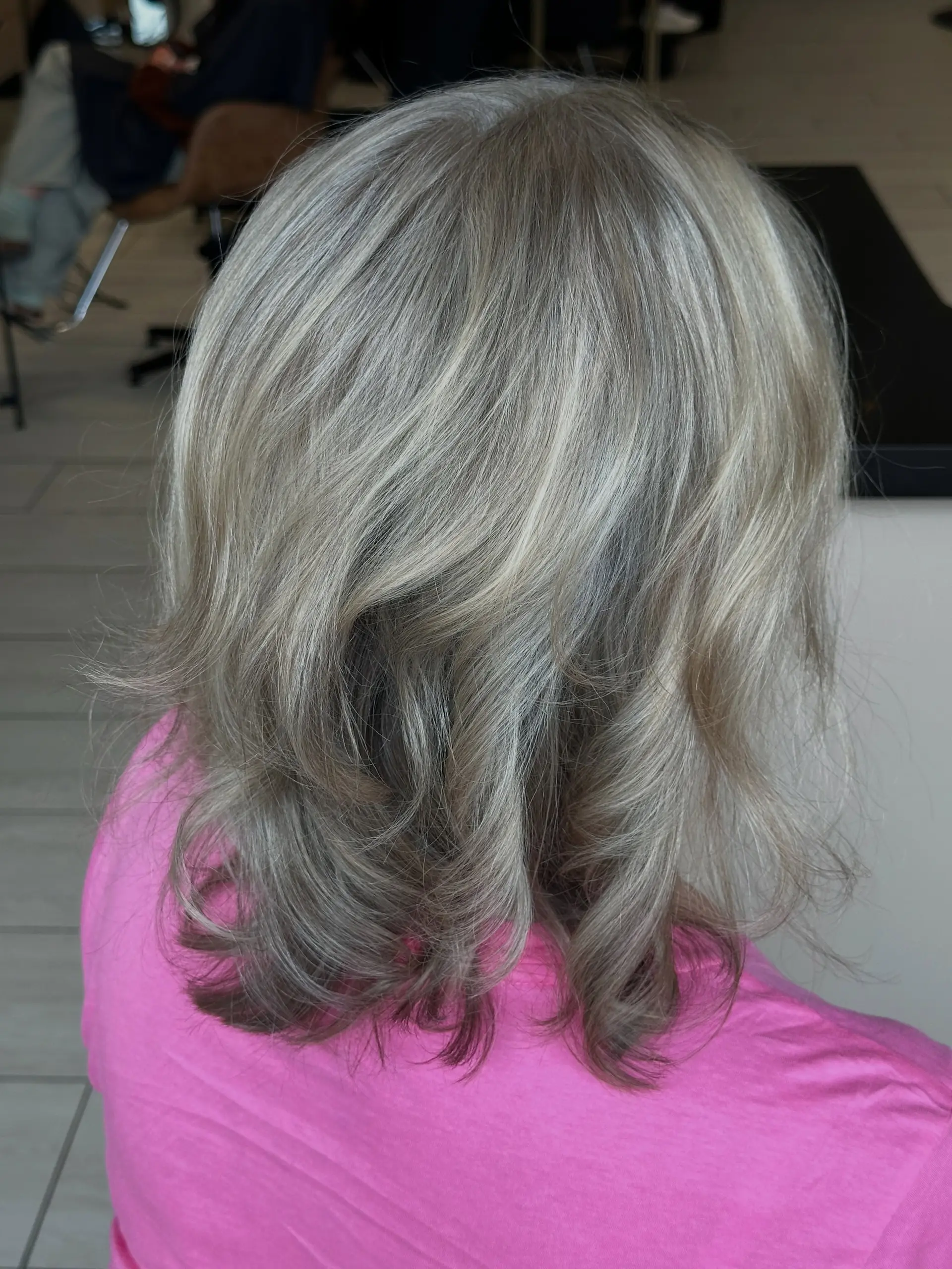 Medium-length layered hairstyle with natural grey blending and ash blonde highlights, finished with soft flips and curls at the ends. 1