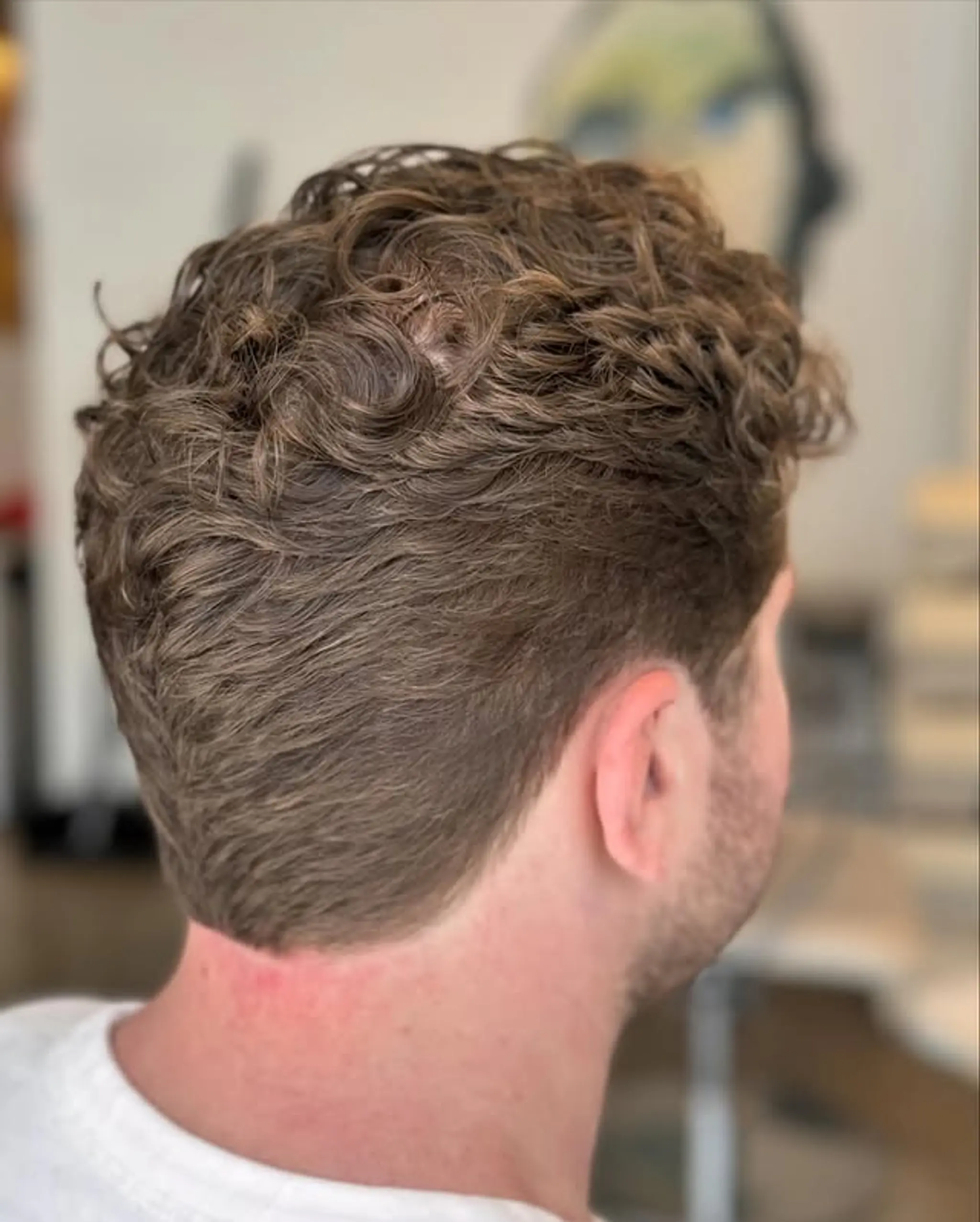 A short, textured curly haircut with a taper fade.