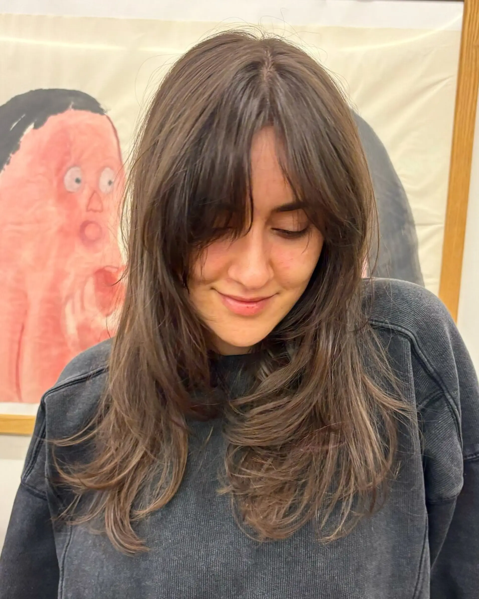 Long, dark brown hair with soft, natural waves and curtain bangs. The style includes face-framing layered tresses that flow down the shoulders, enhancing the hair's natural texture for a casual and elegant appearance. Haircut by @takeohair 1