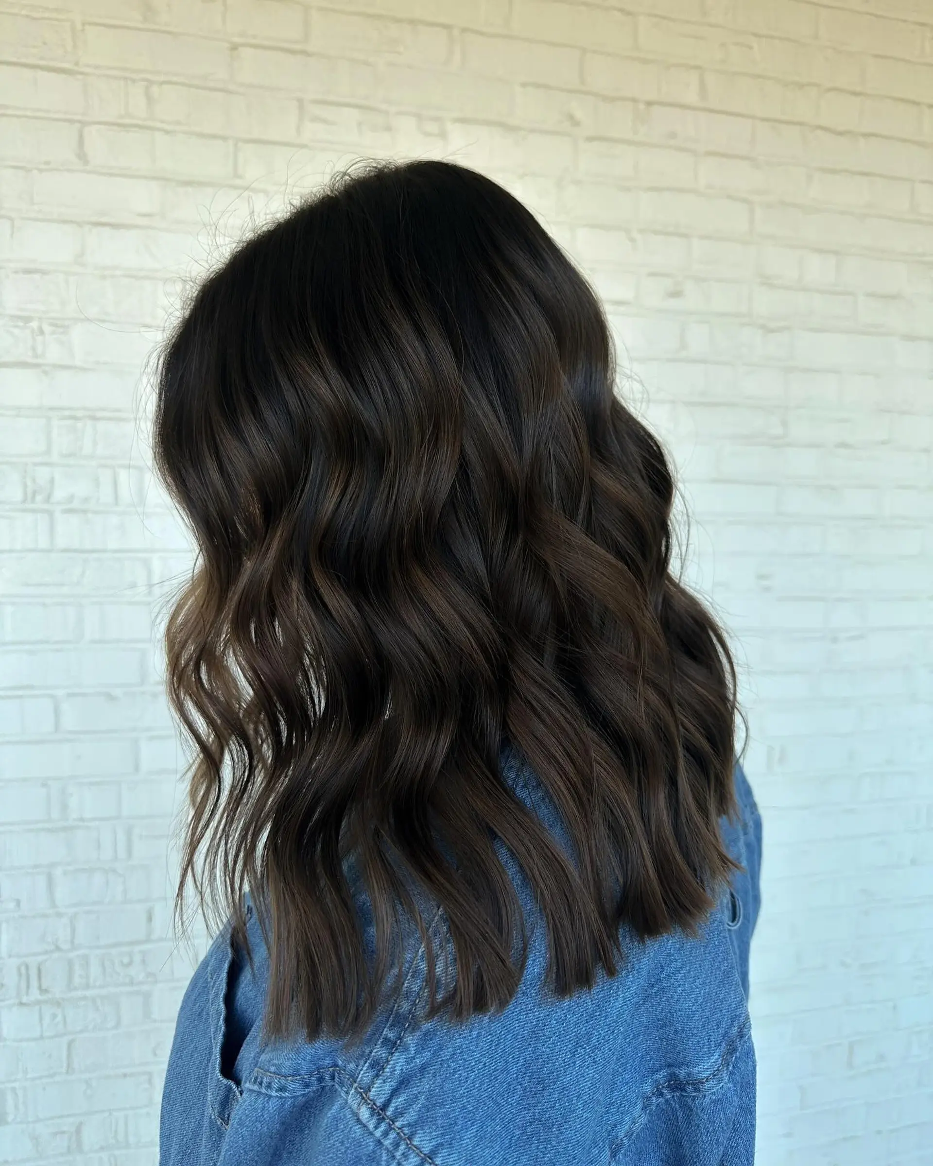 Shoulder-length rich dark brunette hair styled in glossy, defined loose waves. 1