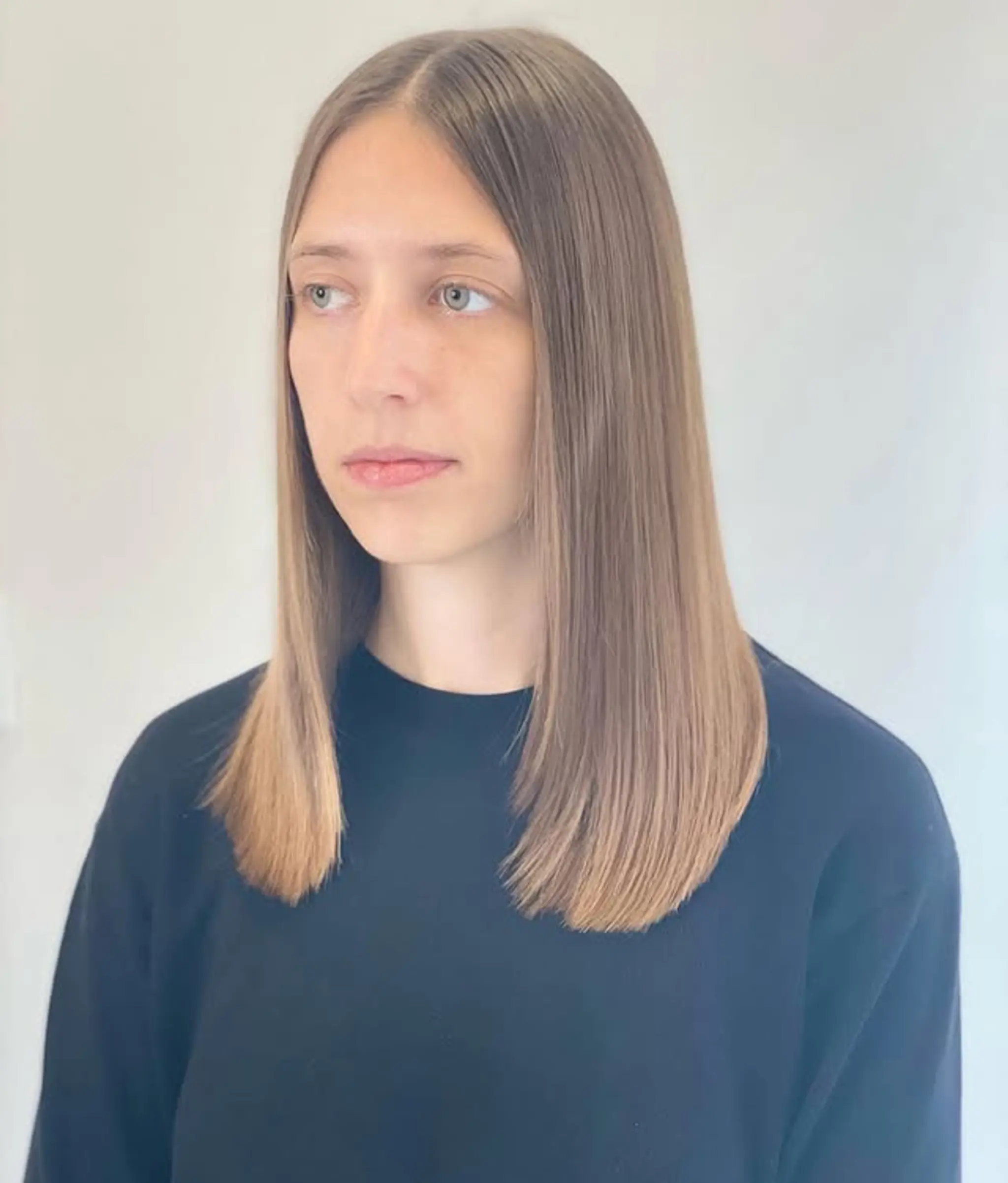 A sleek, straight medium-length hairstyle with subtle face-framing layers and a balayage that transitions from brunette to a soft blonde.