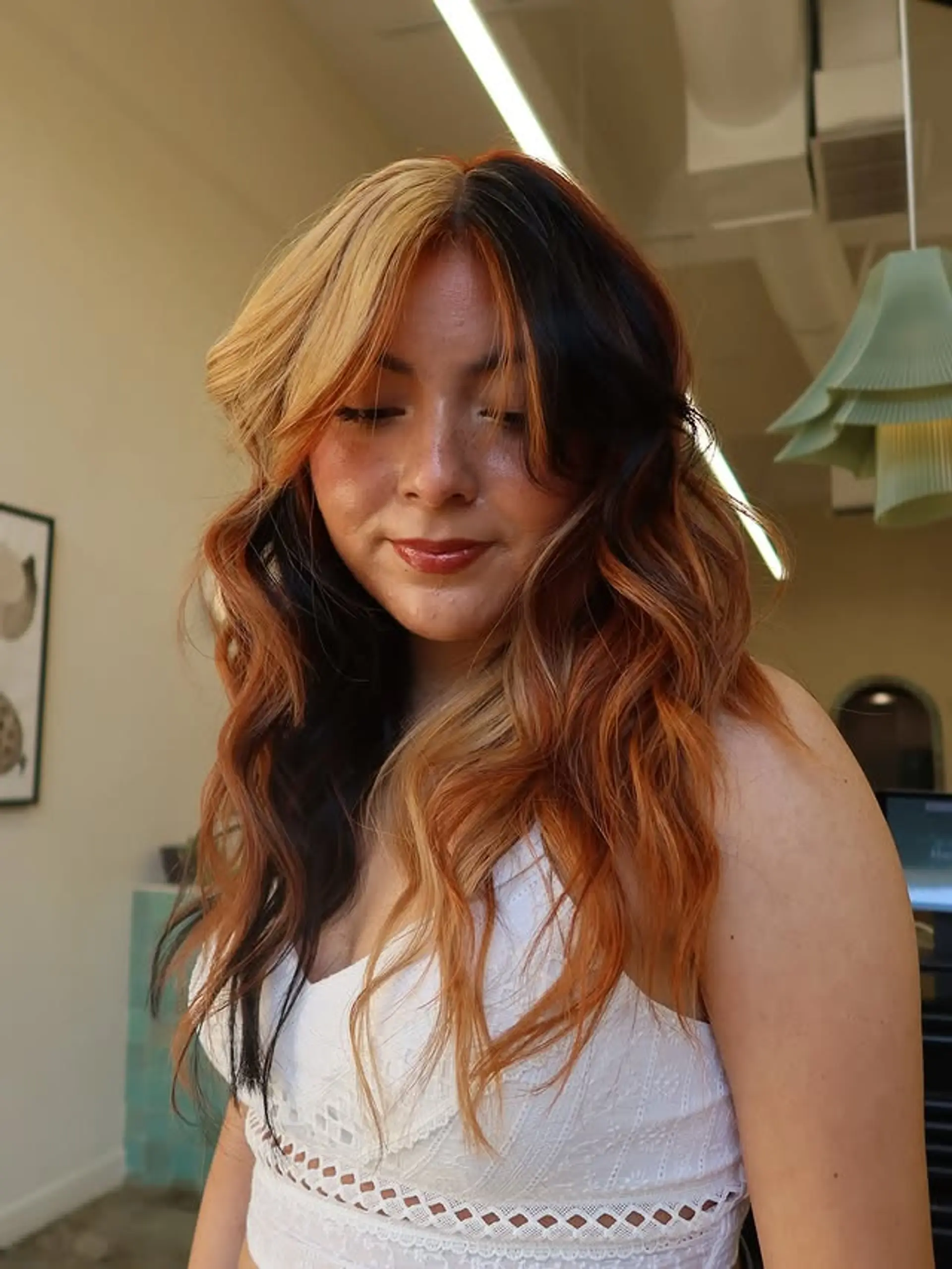 This hairstyle features a vibrant split dye with copper and blonde highlights, enhancing the natural waves and face-framing layers for a trendy, dimensional look. 1