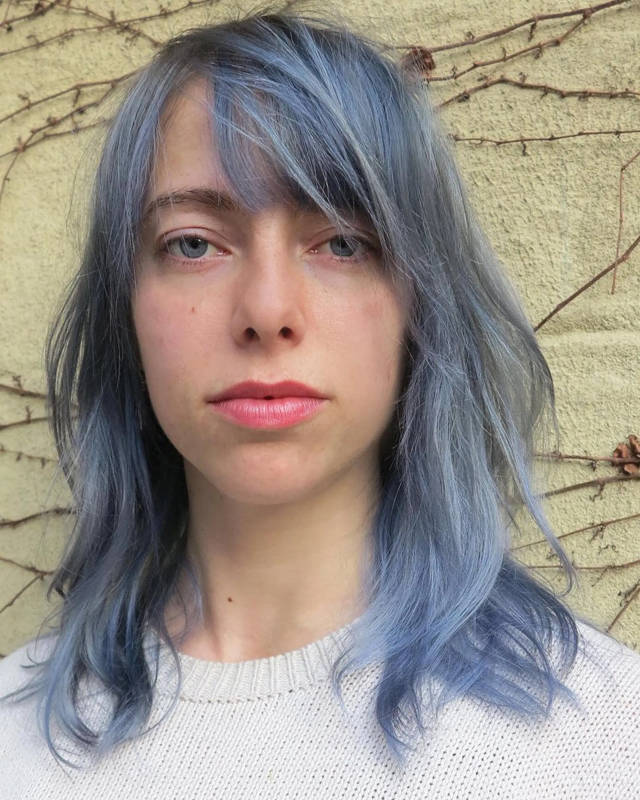 Medium-length wavy hair with a muted blue hue, featuring side bangs and layered texture for a chic look.