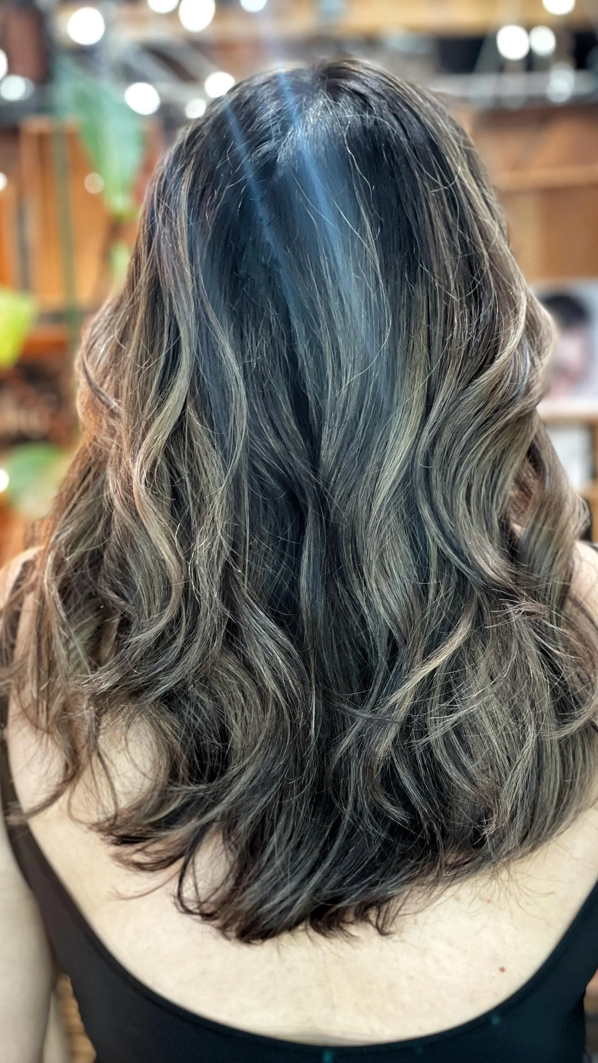 Long dark hair styled into soft, tousled waves with cool ash brown and subtle blonde dimensional balayage. 1