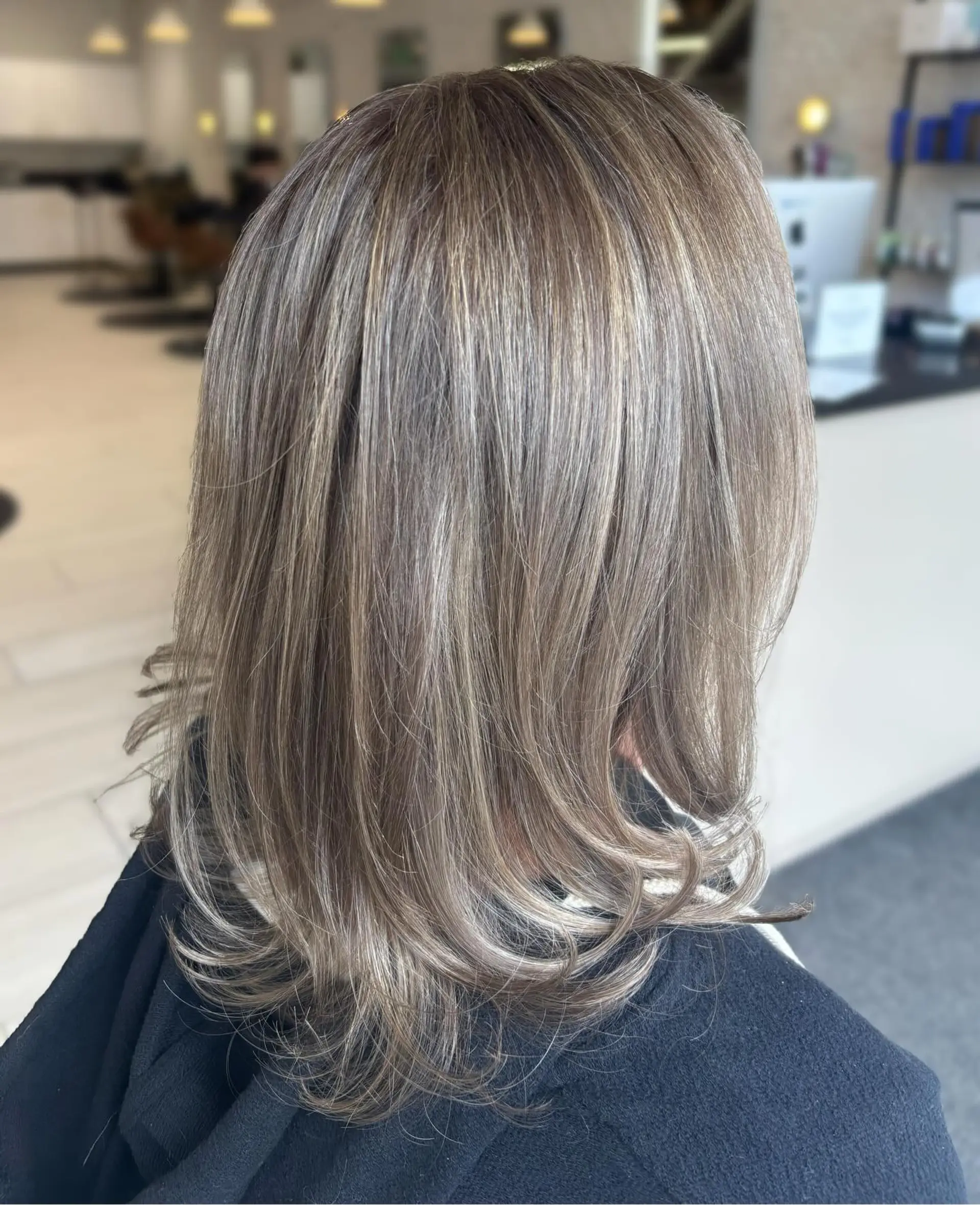 Medium-length dimensional ash blonde hair styled straight with softly flipped ends. 1