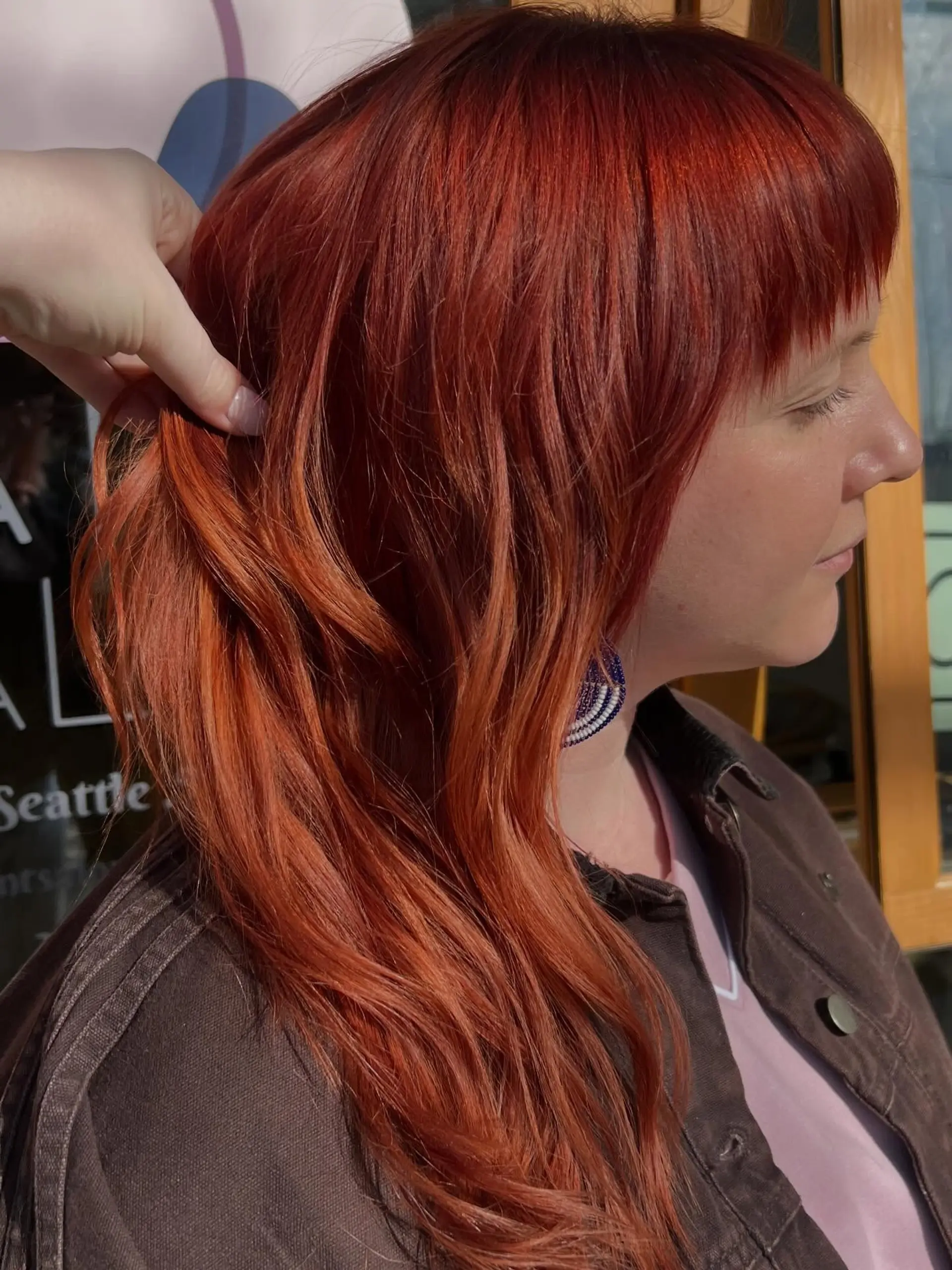 A bright copper red long haircut featuring soft waves and blunt fringe bangs. 1