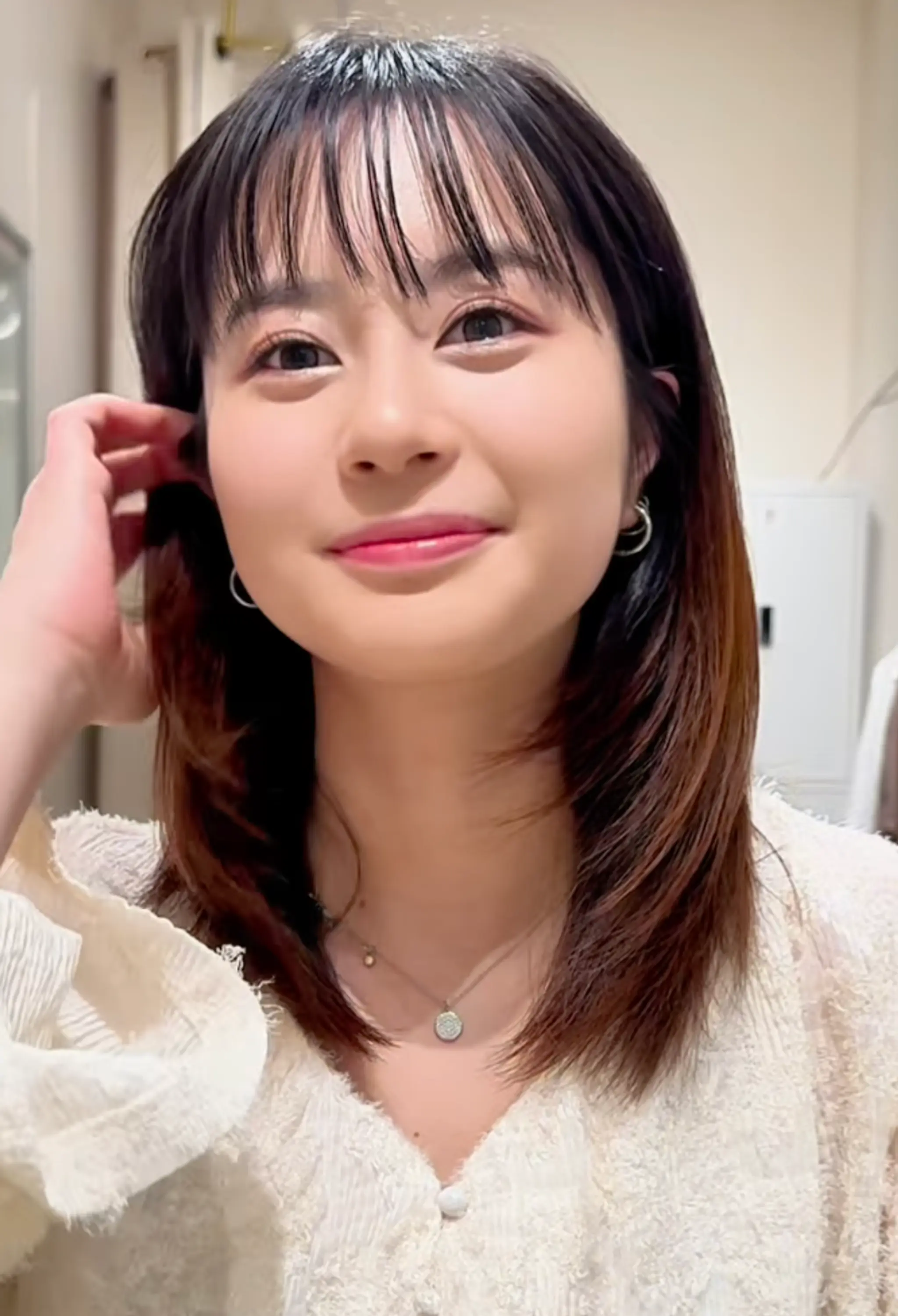Medium-length, straight hair with wispy bangs and soft, elegant layers. The hair features a natural shine with black and brown hues, providing a youthful and sophisticated look.