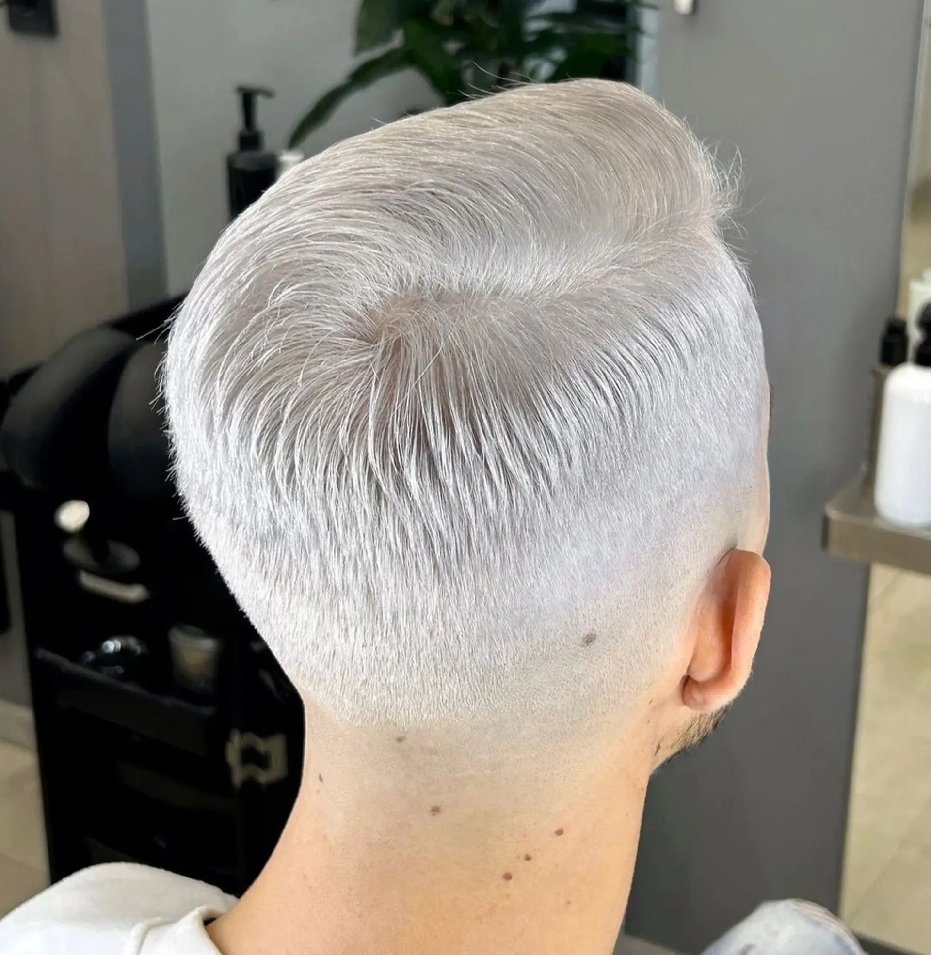A high fade cut with a slicked back, textured top in platinum blonde, featuring clean, sharp lines and a modern finish. 1
