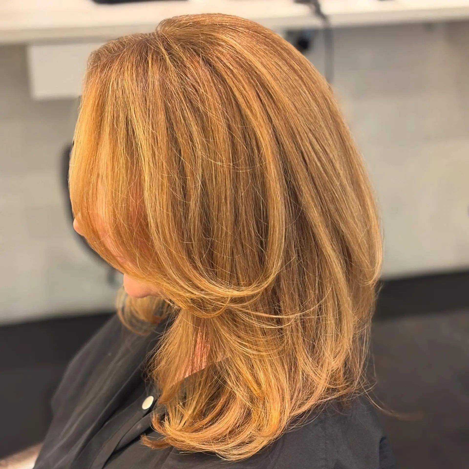 A sleek, voluminous mid-length blowout featuring soft curved face-framing layers in rich honey blonde. 1