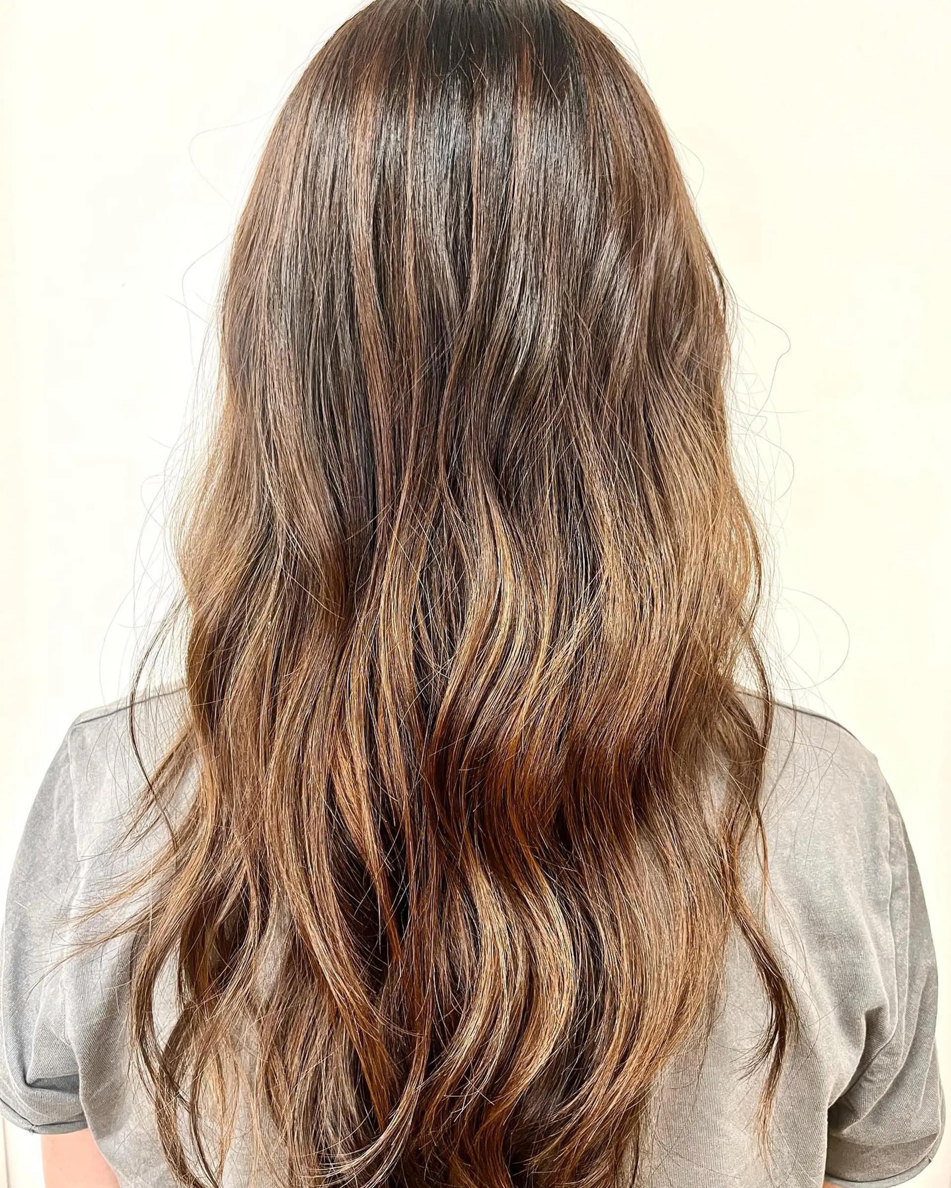 Long dimensional brunette hair styled in loose, soft waves with subtle caramel balayage highlights. 1