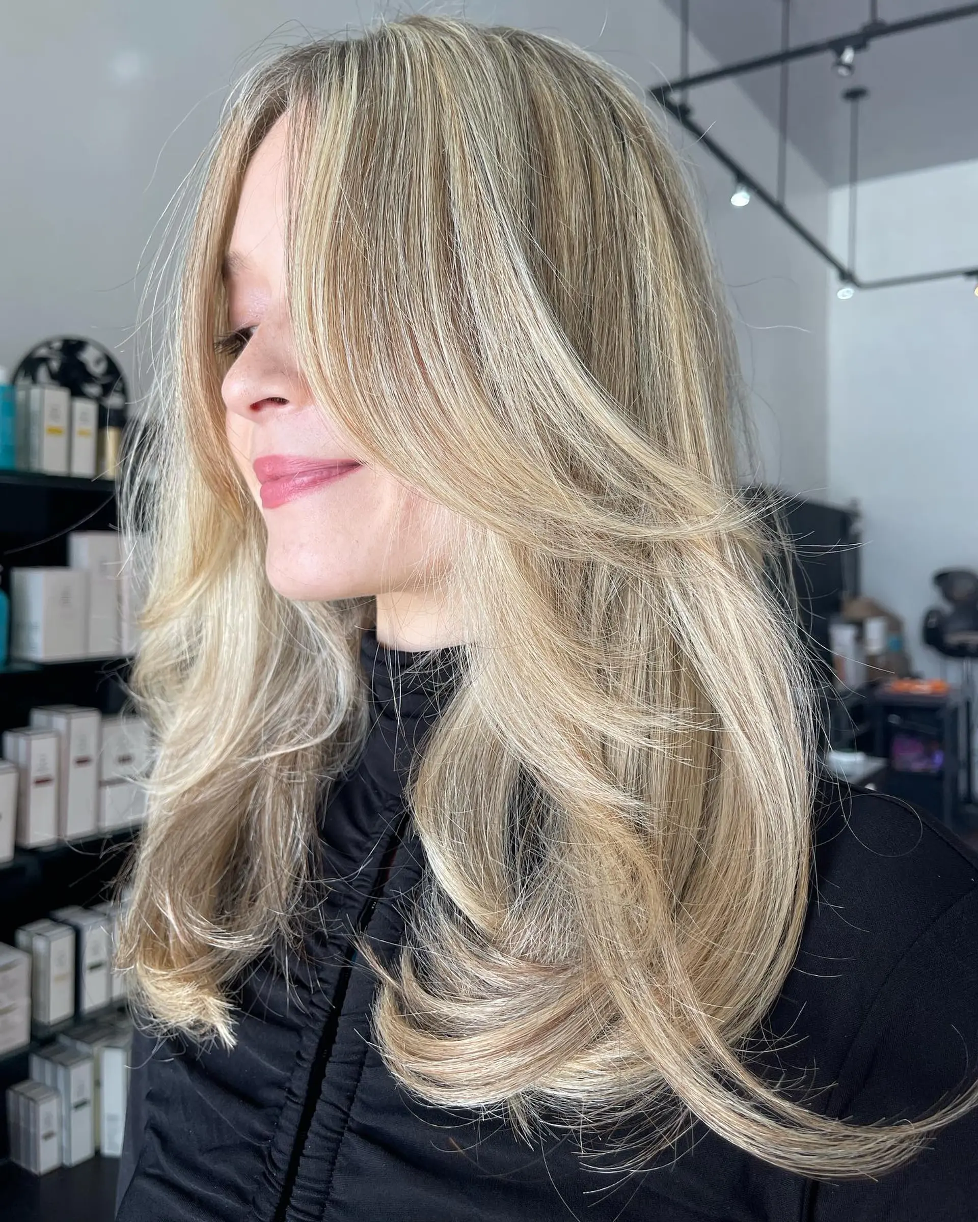 Long dimensional blonde hair styled with a butterfly haircut featuring face-framing layers and a bouncy blowout. 1