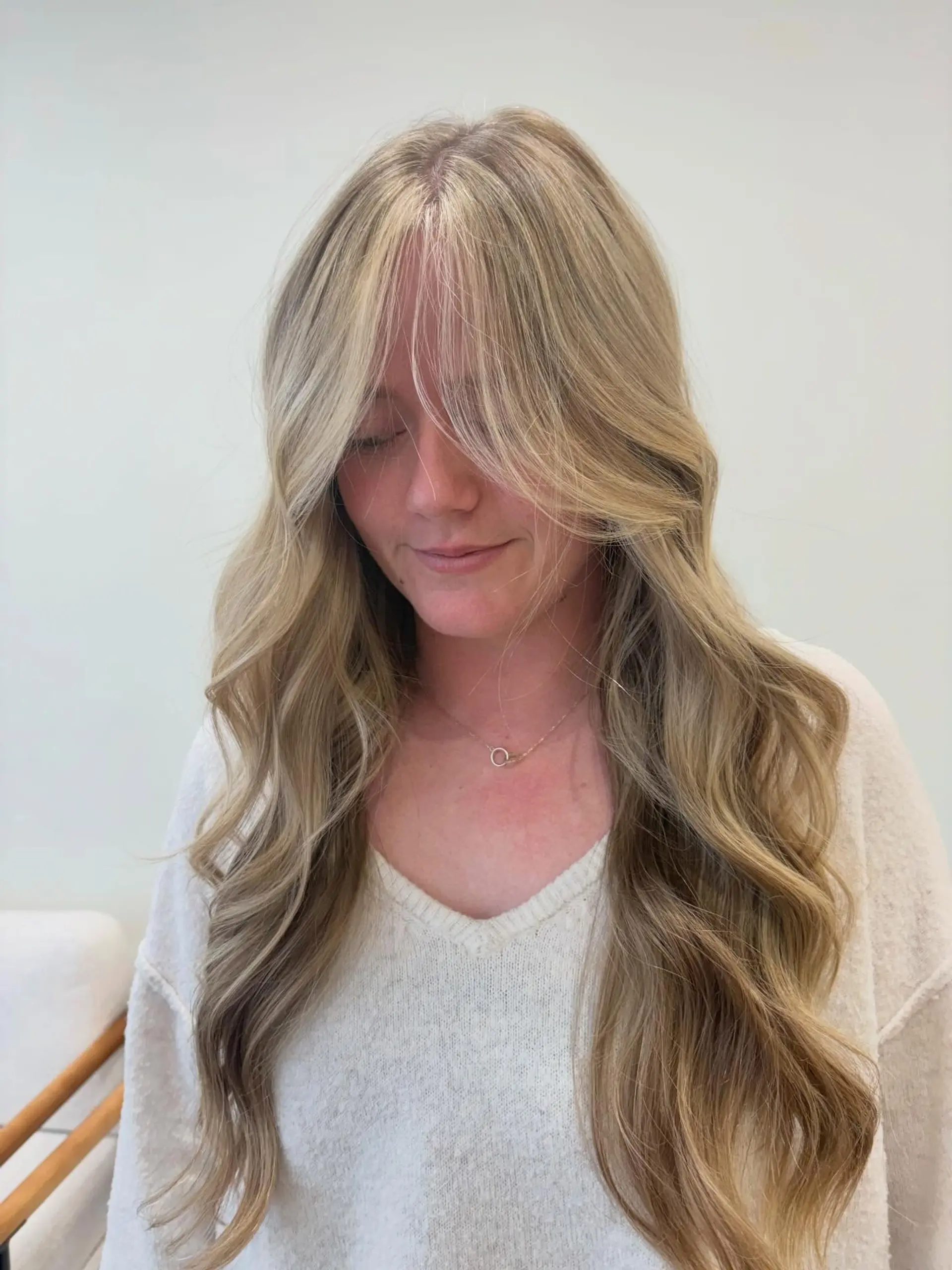 Long dimensional blonde hair styled in soft, loose waves with face-framing curtain bangs. 1