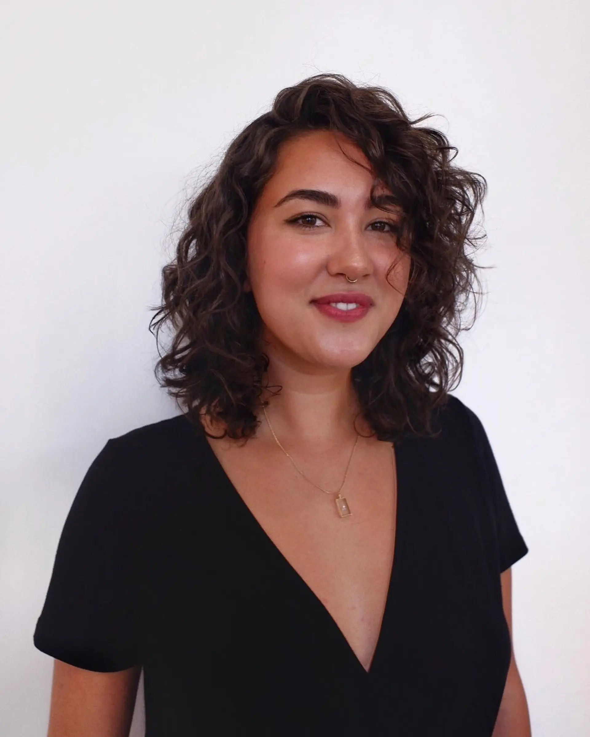 A shoulder-length naturally curly haircut with bouncy volume and a side part. 1