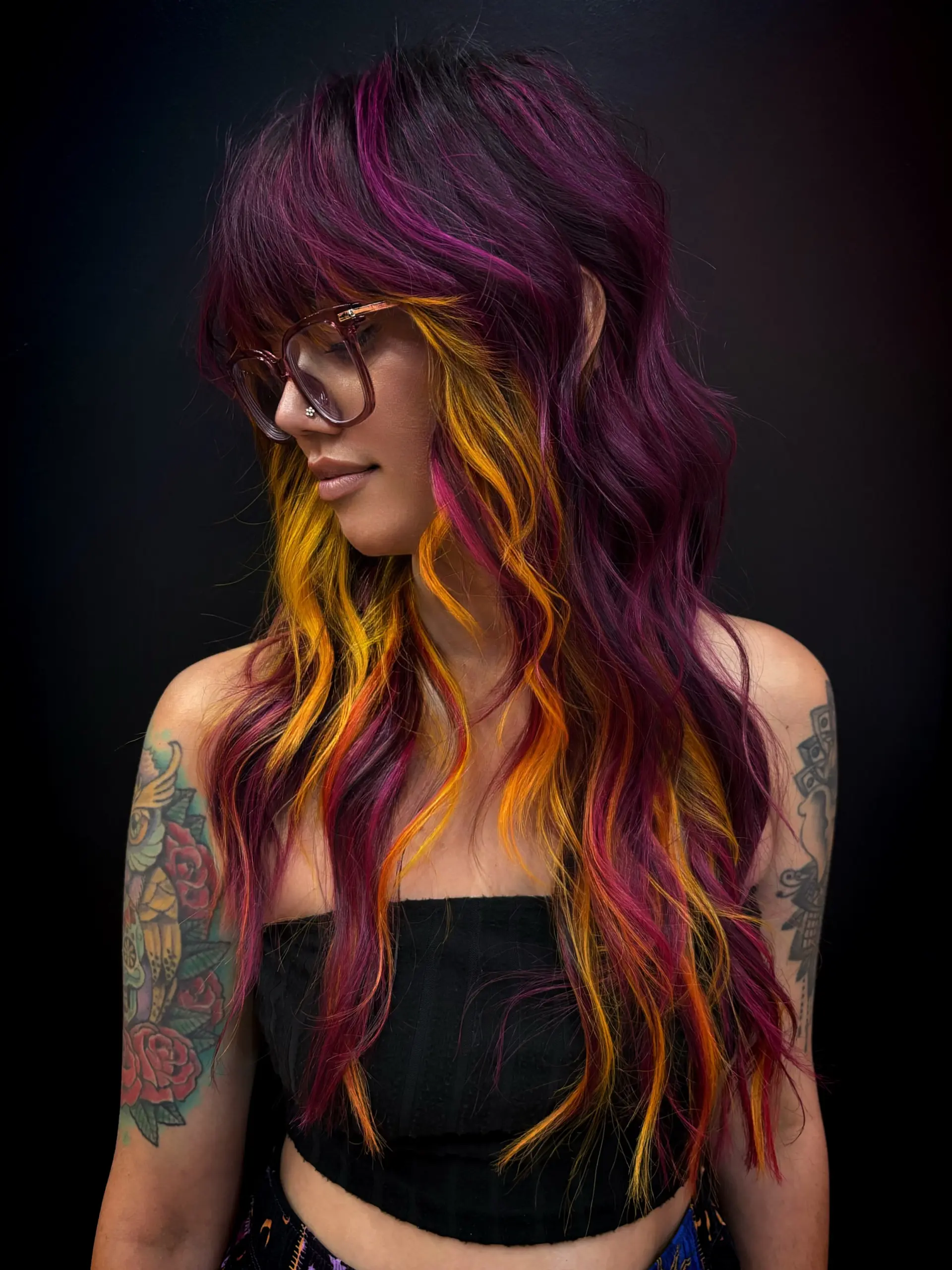 A layered long shag with full bangs styled in soft waves, featuring deep magenta-purple with vibrant yellow and orange peekaboo accents. 1