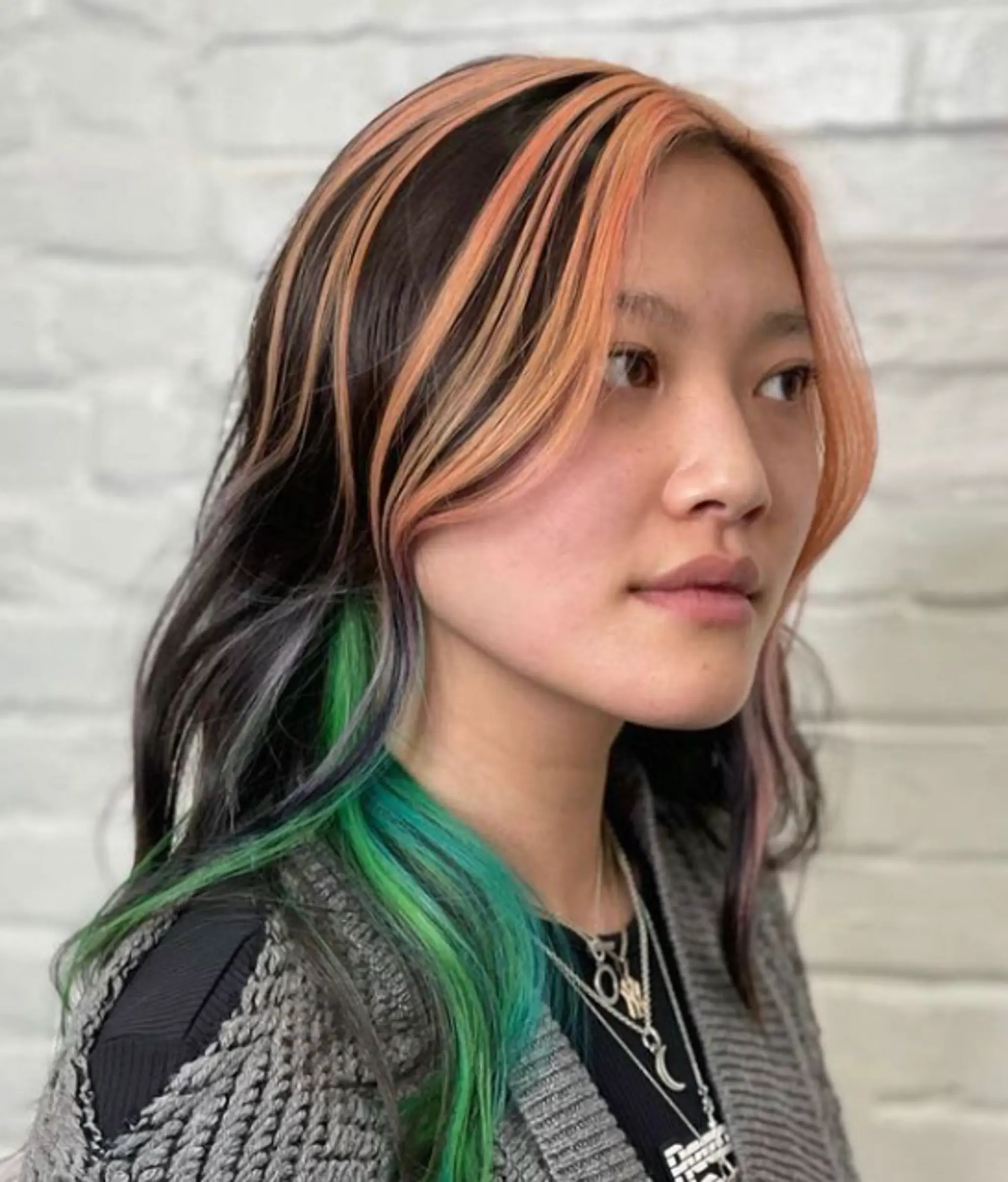 A vibrant multicolored, layered cut with black, orange, green, and pink tones. The hair is straight and medium-length, parted on the side with face-framing layers.