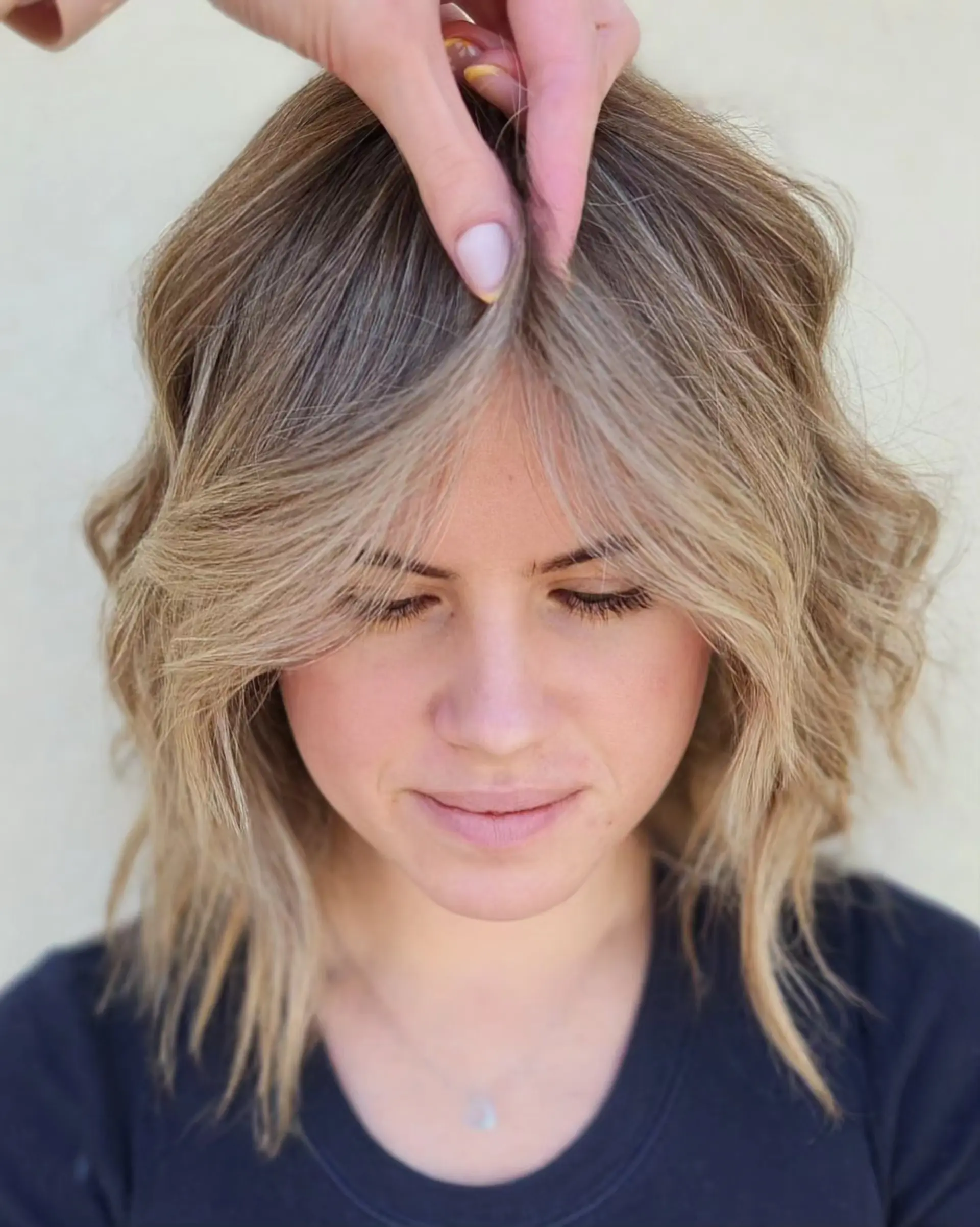A textured shoulder-length lob featuring soft, lived-in blonde balayage highlights and face-framing curtain bangs. 1