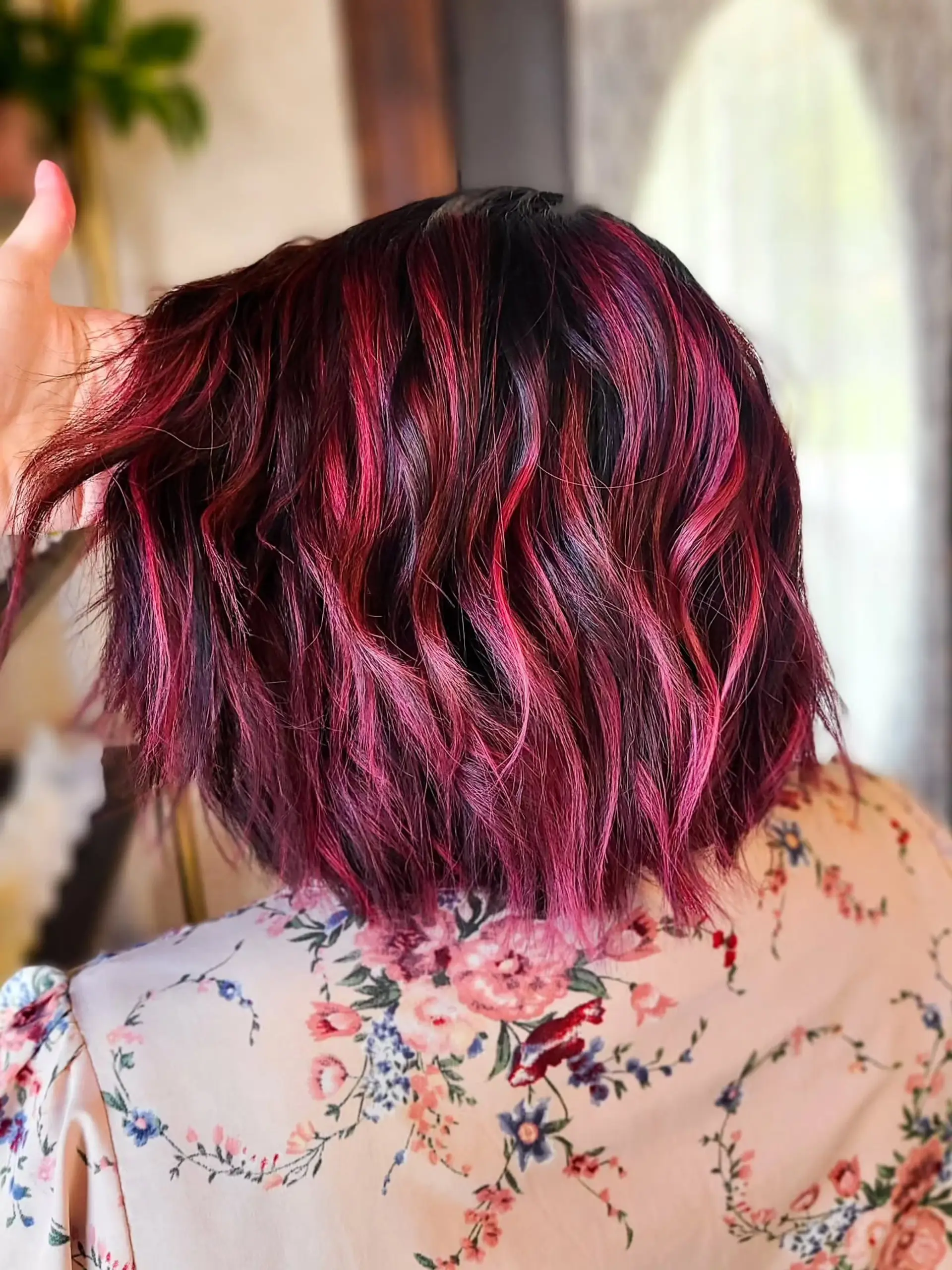A trendy medium-length wavy bob, showcasing dynamic magenta and pink highlights over a dark base, styled with soft, natural waves for a playful yet sophisticated look. 2