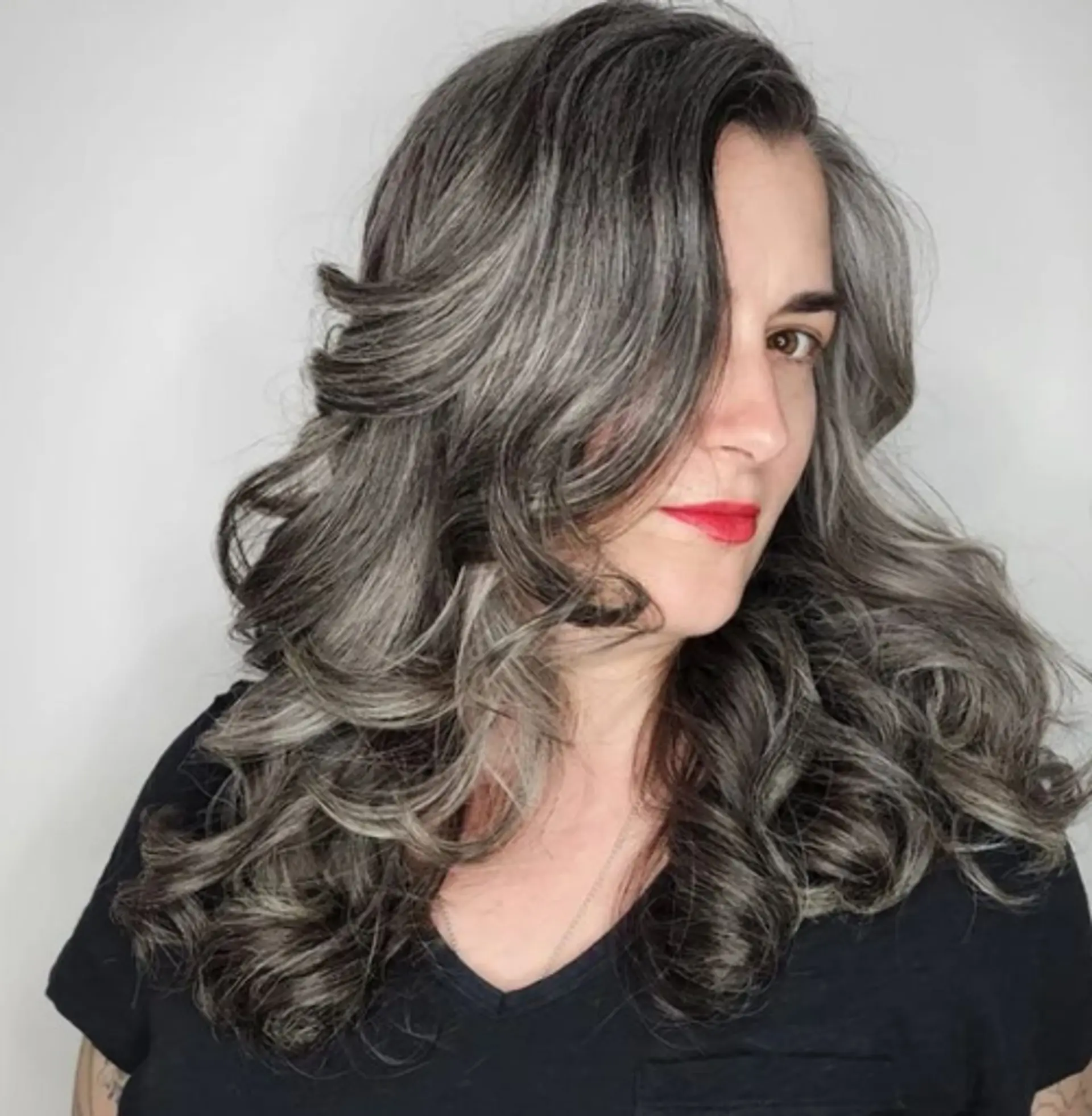 The 'Classic Tousle' features long, wavy hair in silver and dark grey tones with soft curls and voluminous body. 1