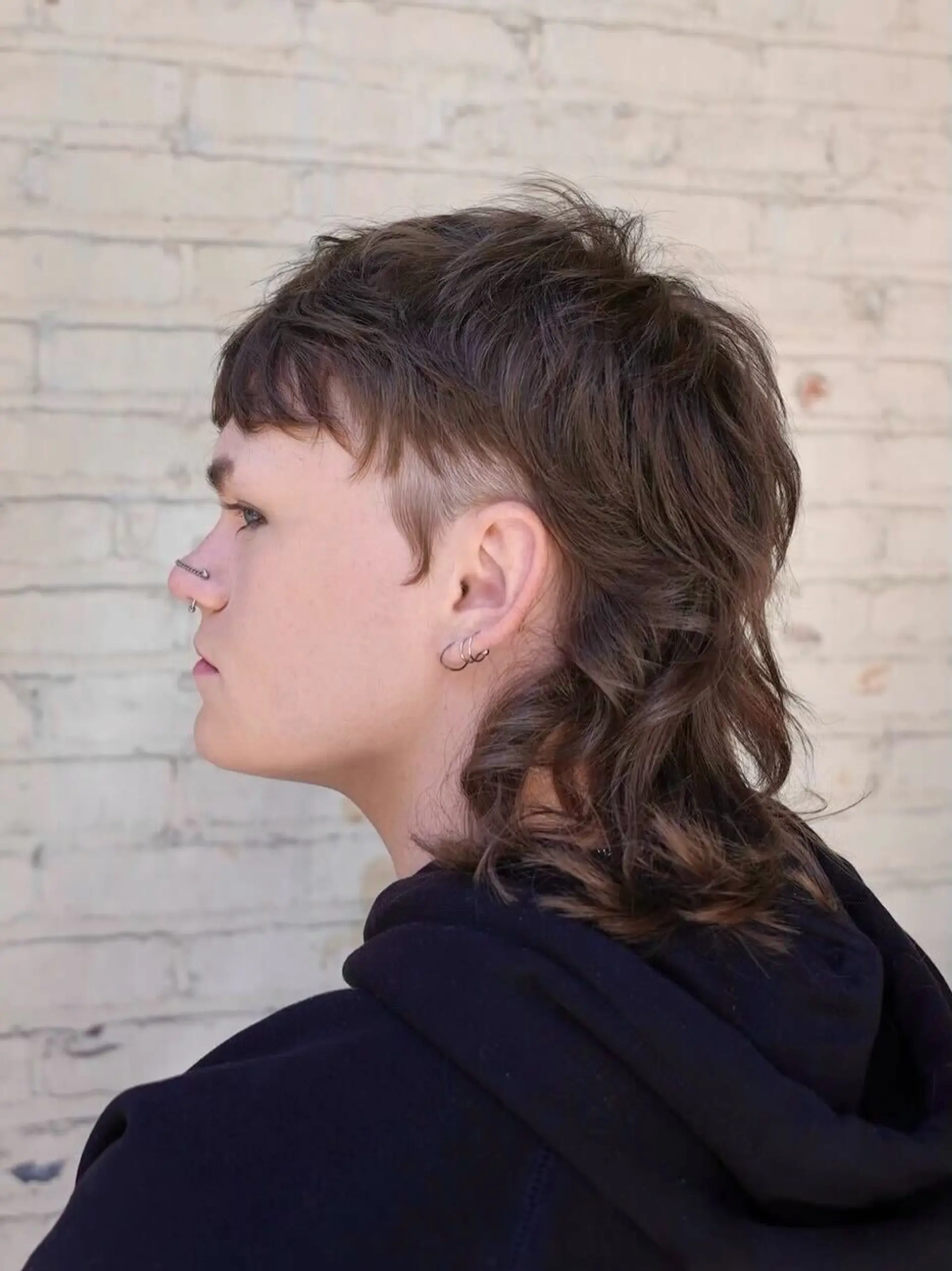 A modern textured mullet haircut with micro fringe, tapered sides above the ear, and layered wavy length in the back. 1