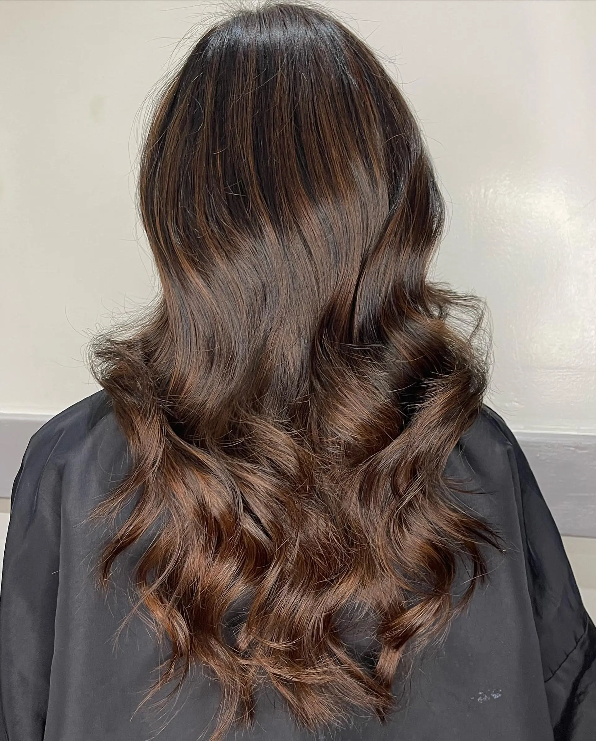 Long dark brown hair enhanced with seamless warm chestnut balayage highlights and styled into loose waves. 1