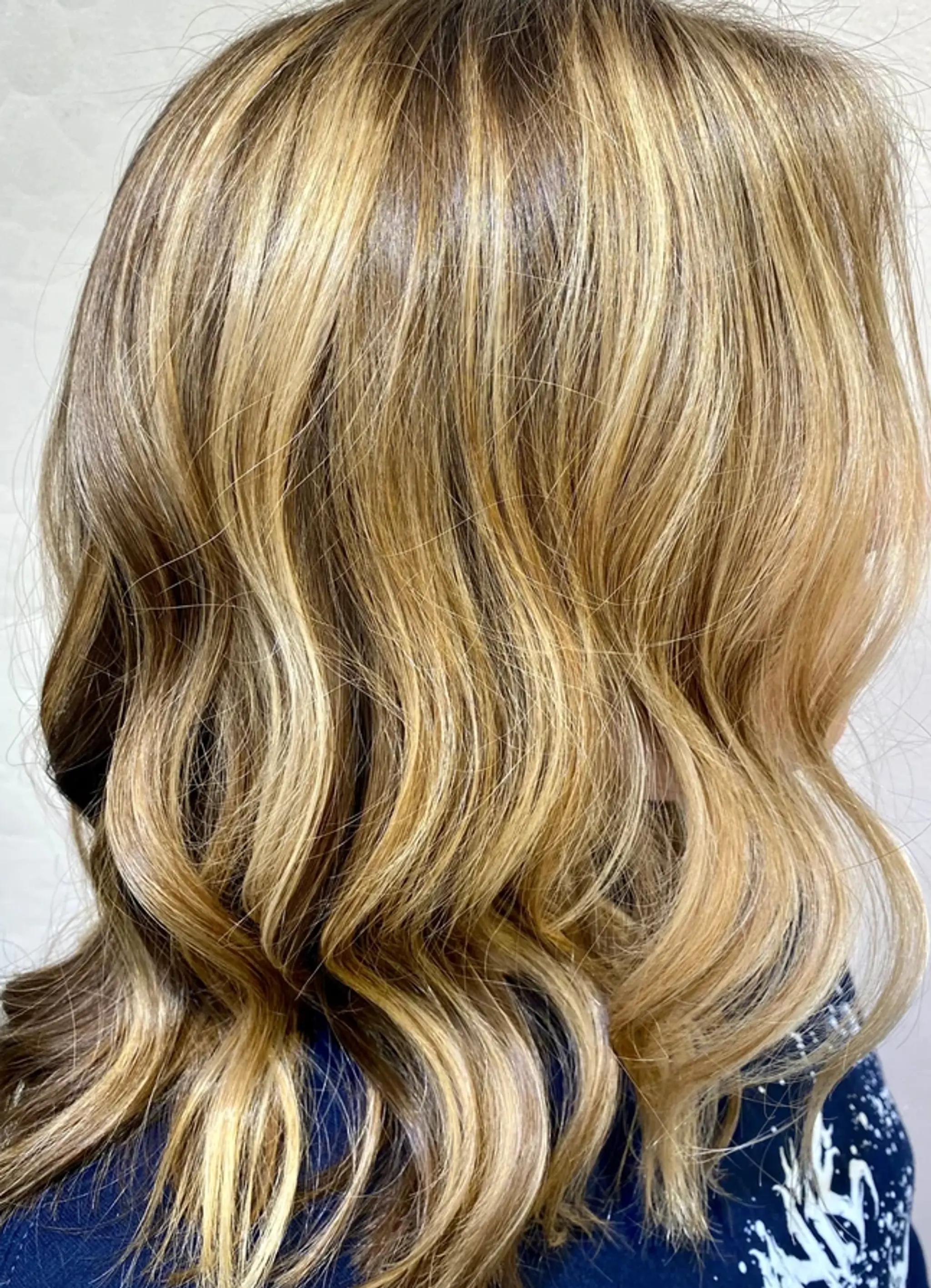 Long wavy hairstyle with golden blonde and honey tones, natural shine, and layered cut.