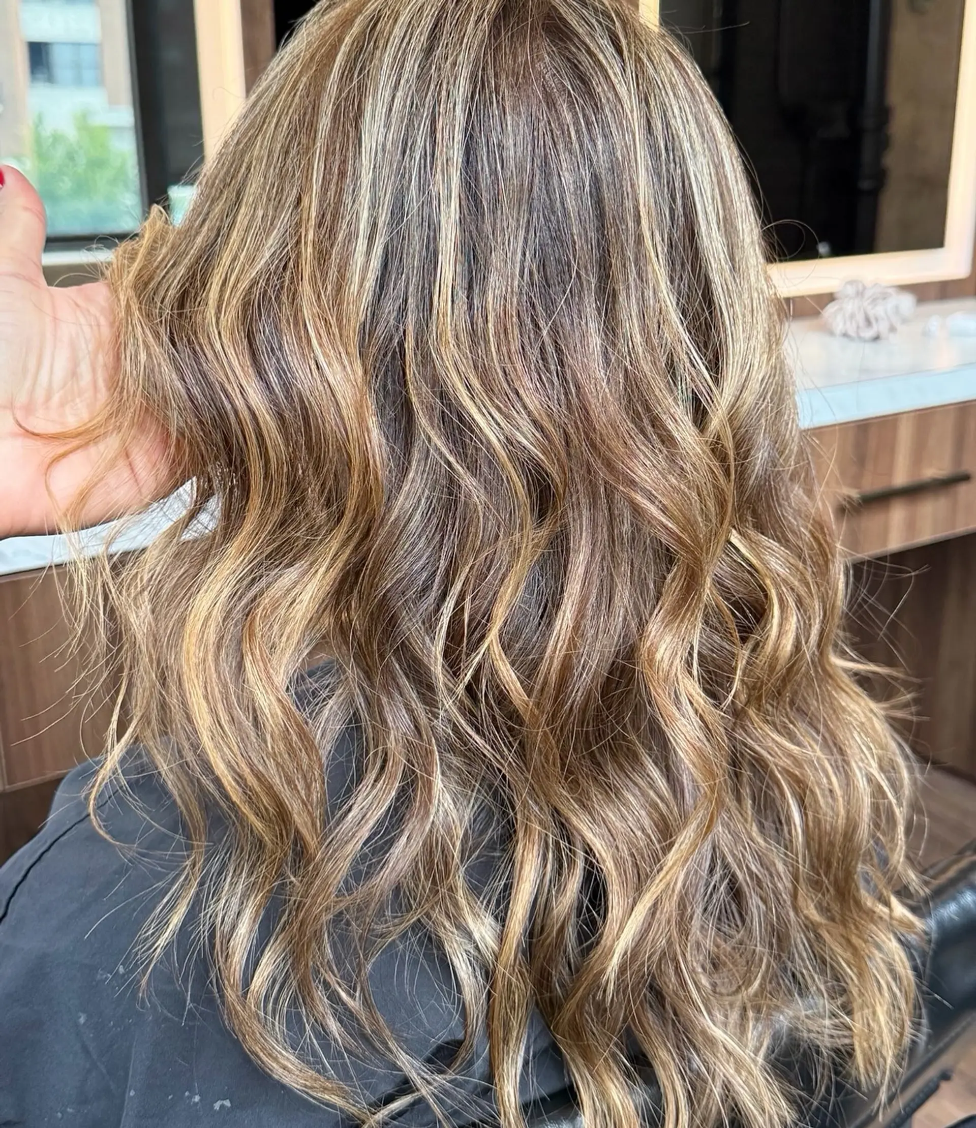 Long dimensional hair colored with fine blonde highlights over a neutral light brown base, styled into textured, cascading beach waves. 1